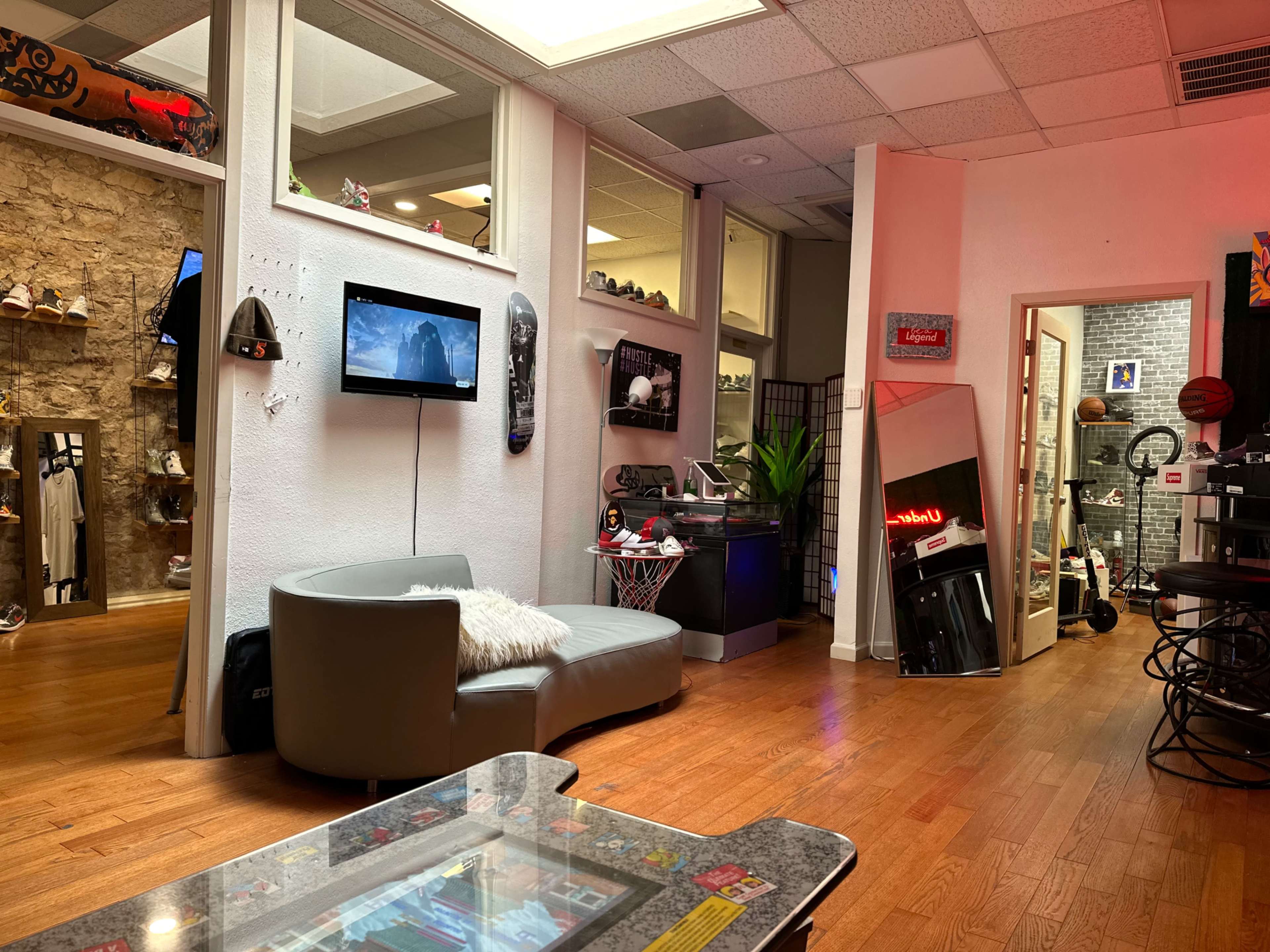 The image shows a stylish room with a gray couch, retro arcade machine, and mirrors across from a television and various items on display.