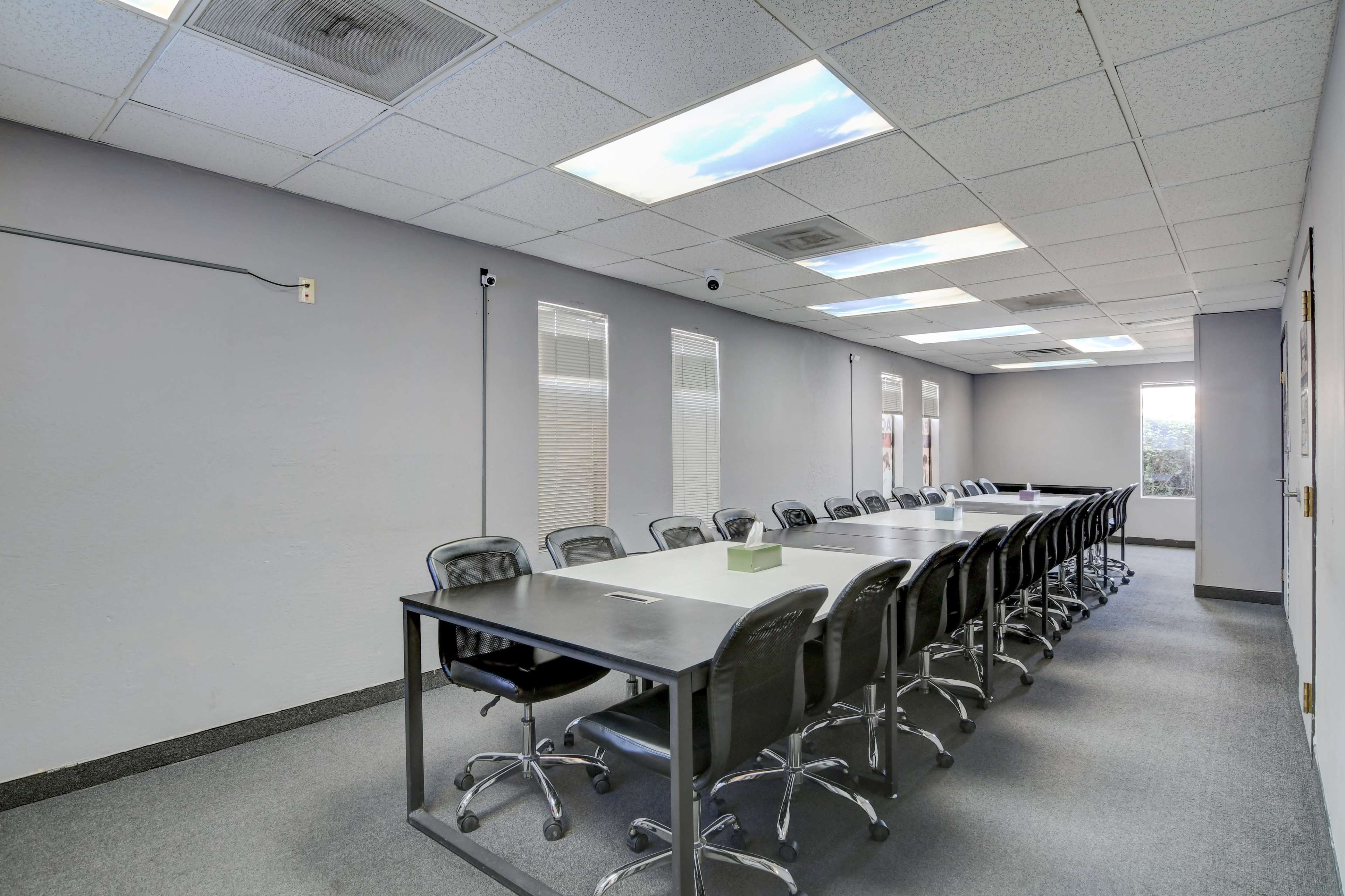 A long conference table surrounded by black office chairs is situated in a room with gray walls and skylights.
