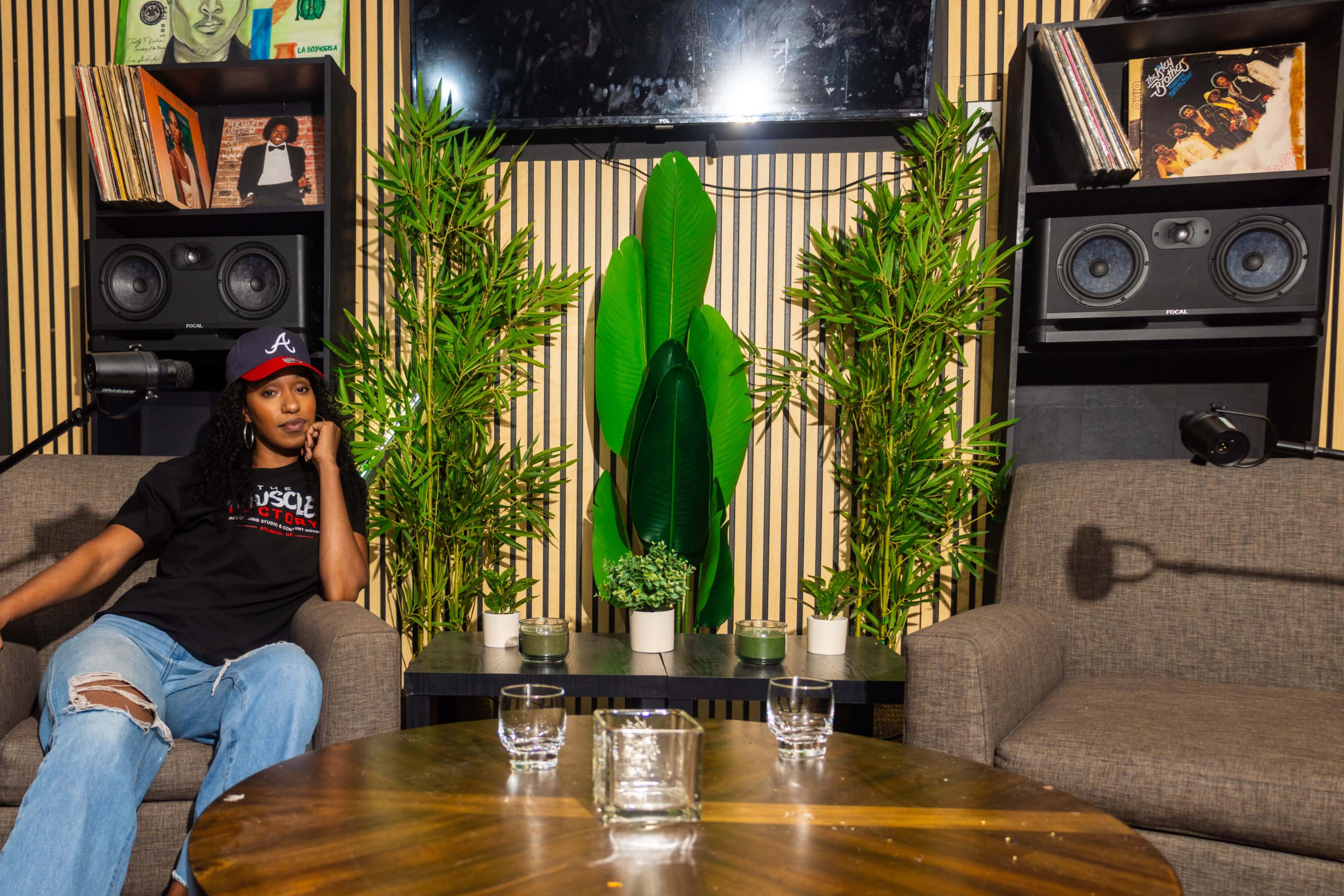 A person sits on a couch in a stylish room decorated with plants, speakers, and vinyl records.