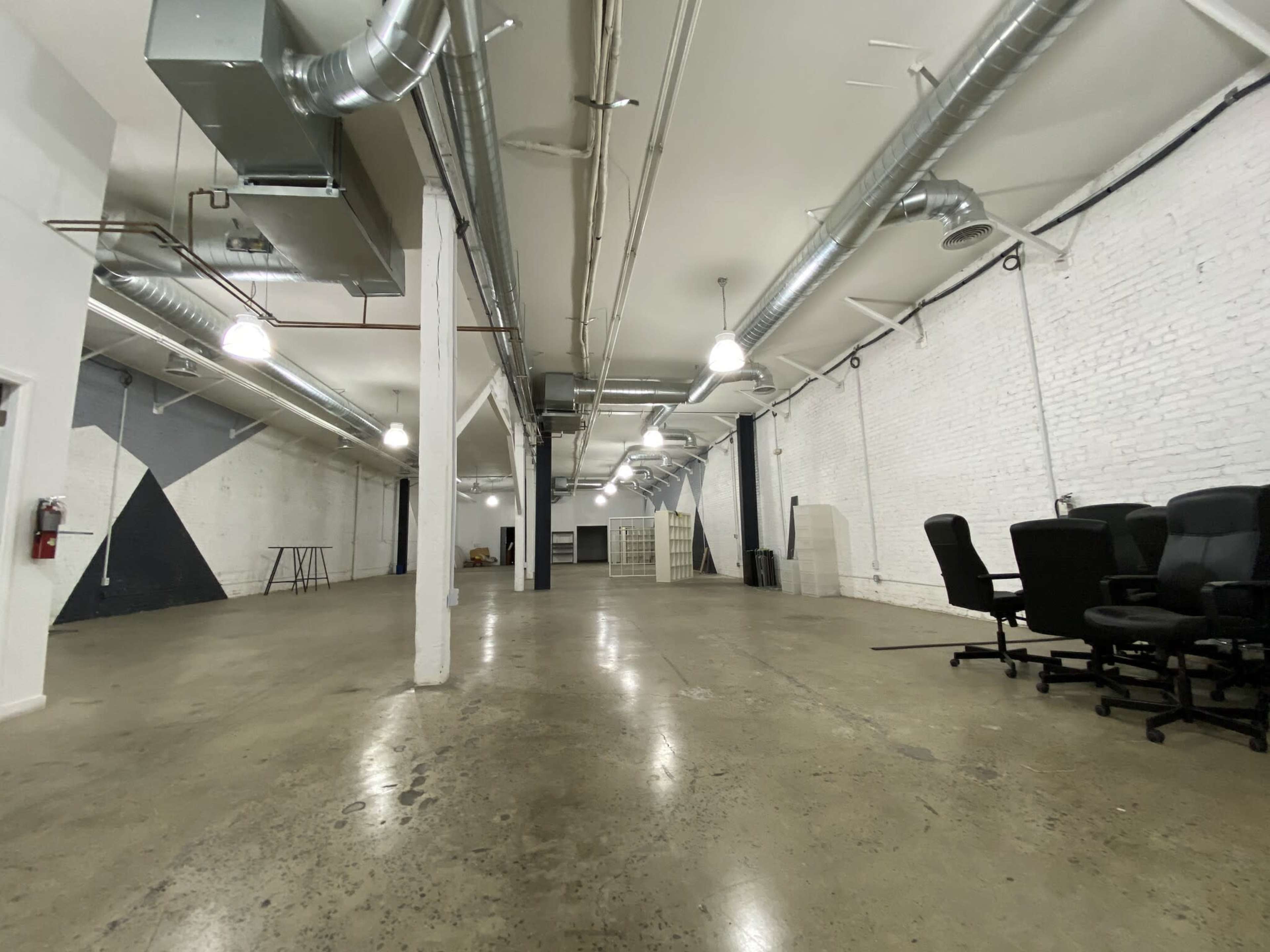 A spacious, unfinished indoor area with white brick walls, concrete flooring, and several office chairs arranged in the foreground.