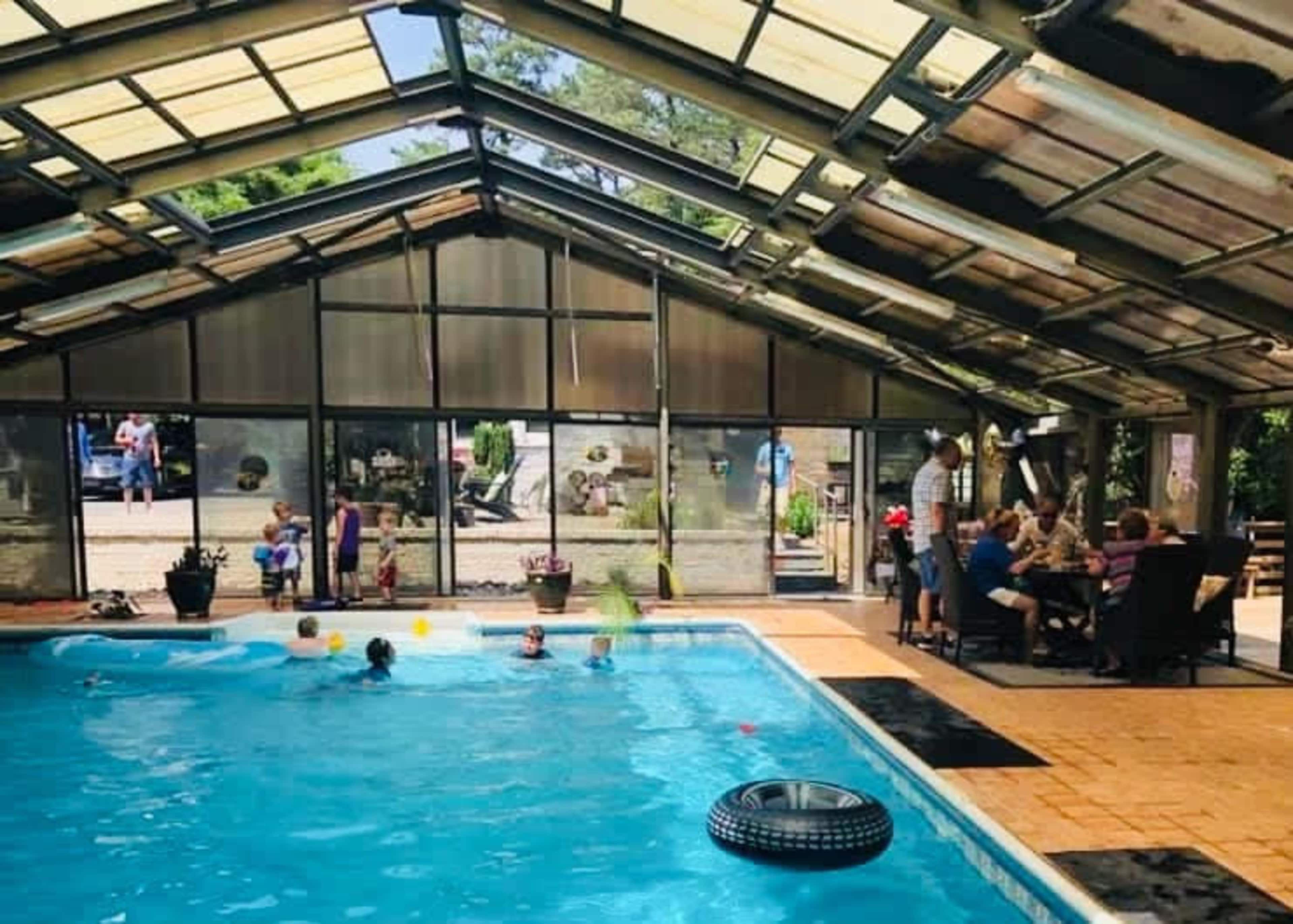 A group of people enjoying a gathering around a swimming pool inside a glass-enclosed structure.