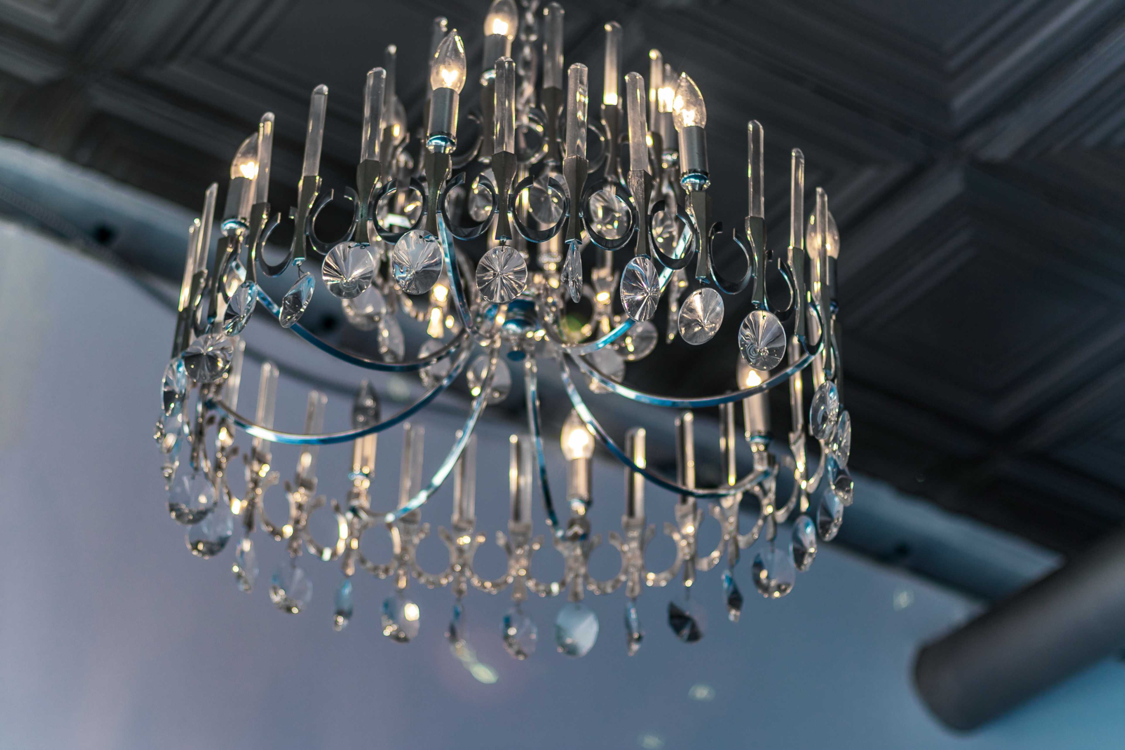 A crystal chandelier with multiple lights hangs from a decorative ceiling.