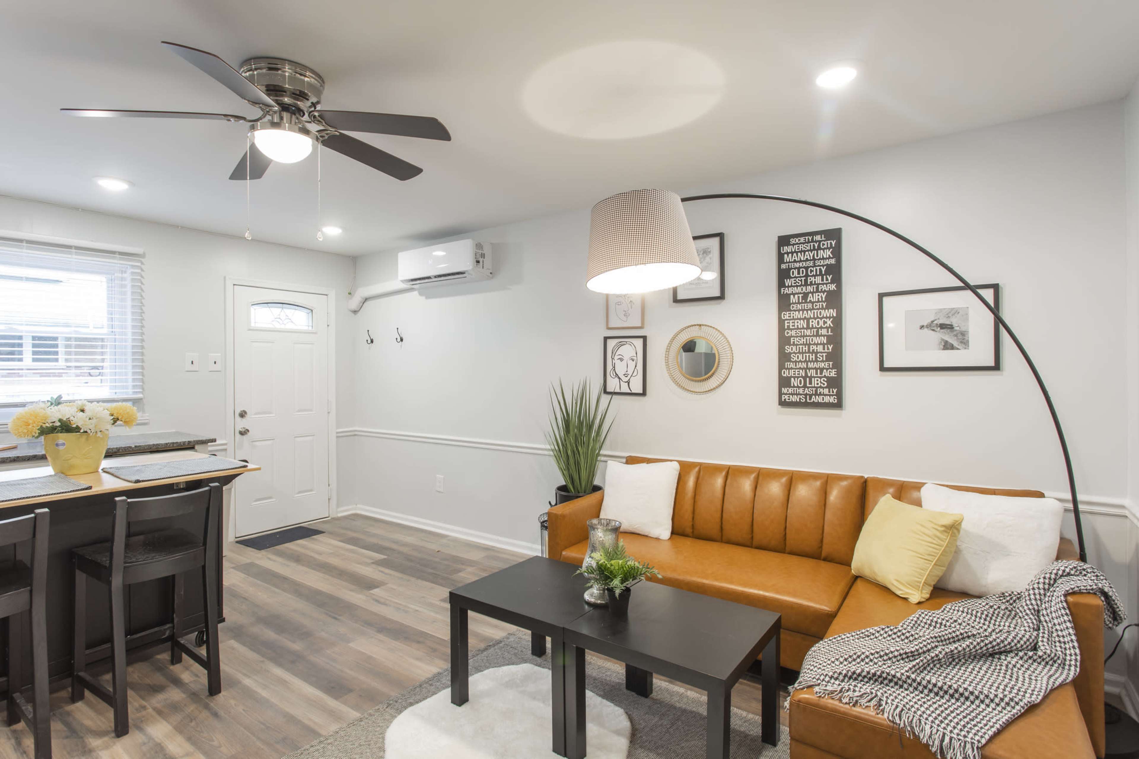 A cozy living room featuring a brown leather sofa, a black coffee table, and a ceiling fan, with a door leading outside and a dining area in the background.