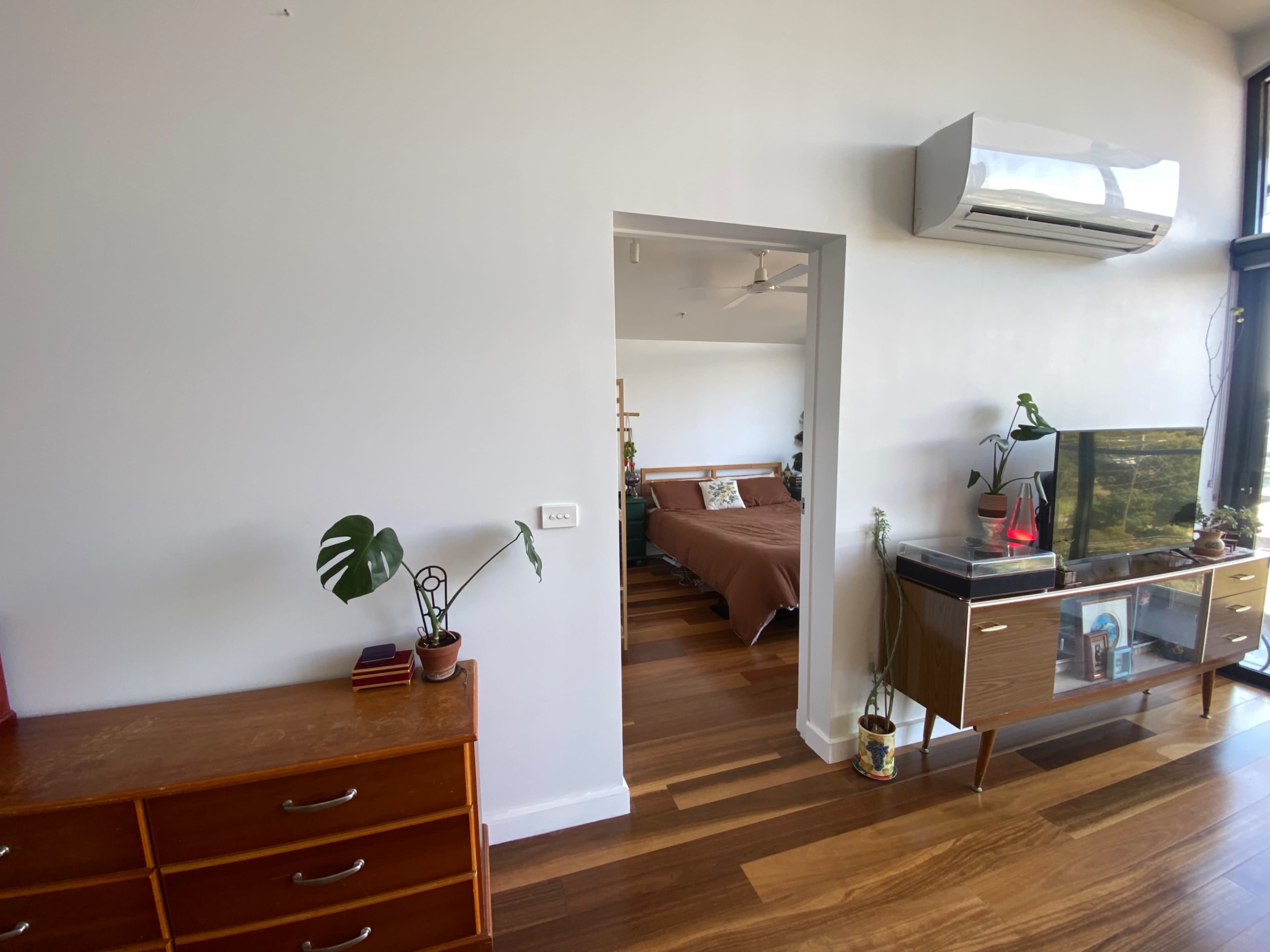 A hallway leads from a wooden dresser to a living area with a bed and a television.