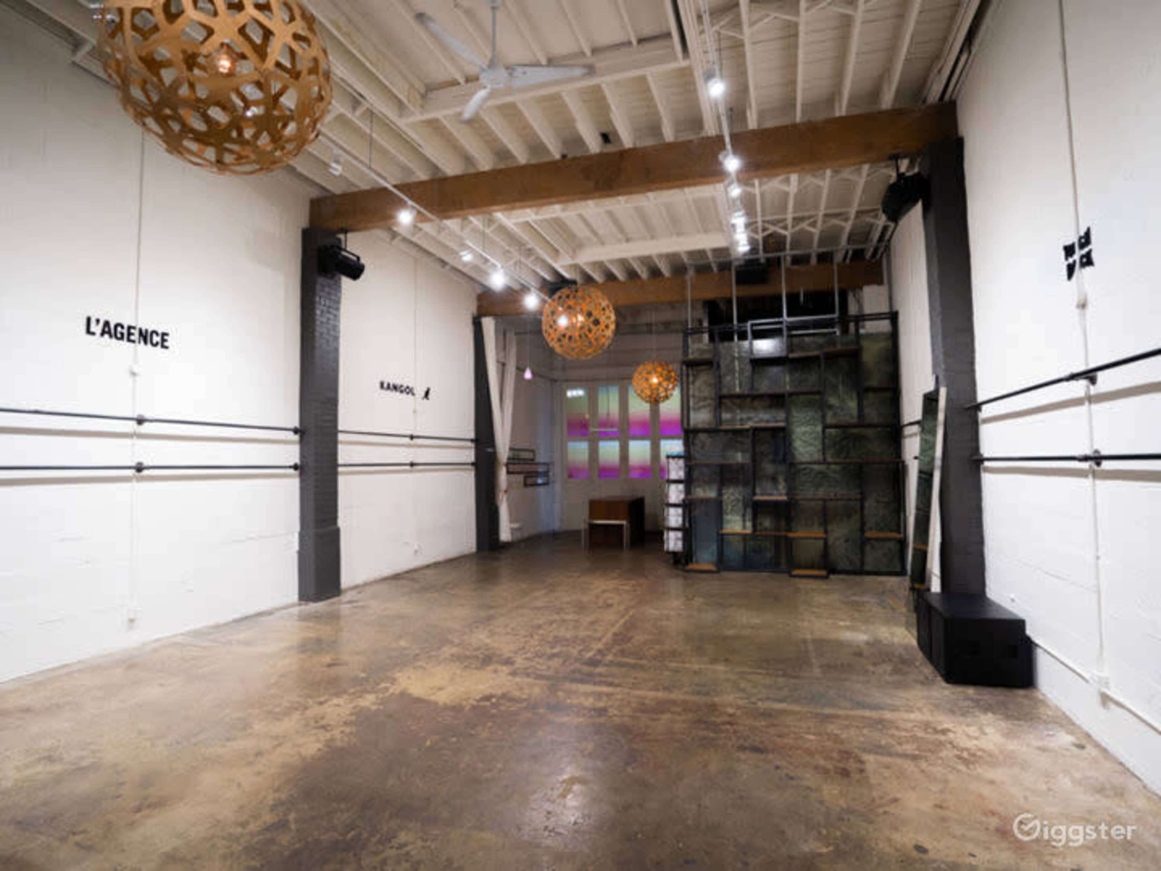A spacious, modern interior with wooden beams, concrete floors, and decorative pendant lights, featuring a minimalist design.
