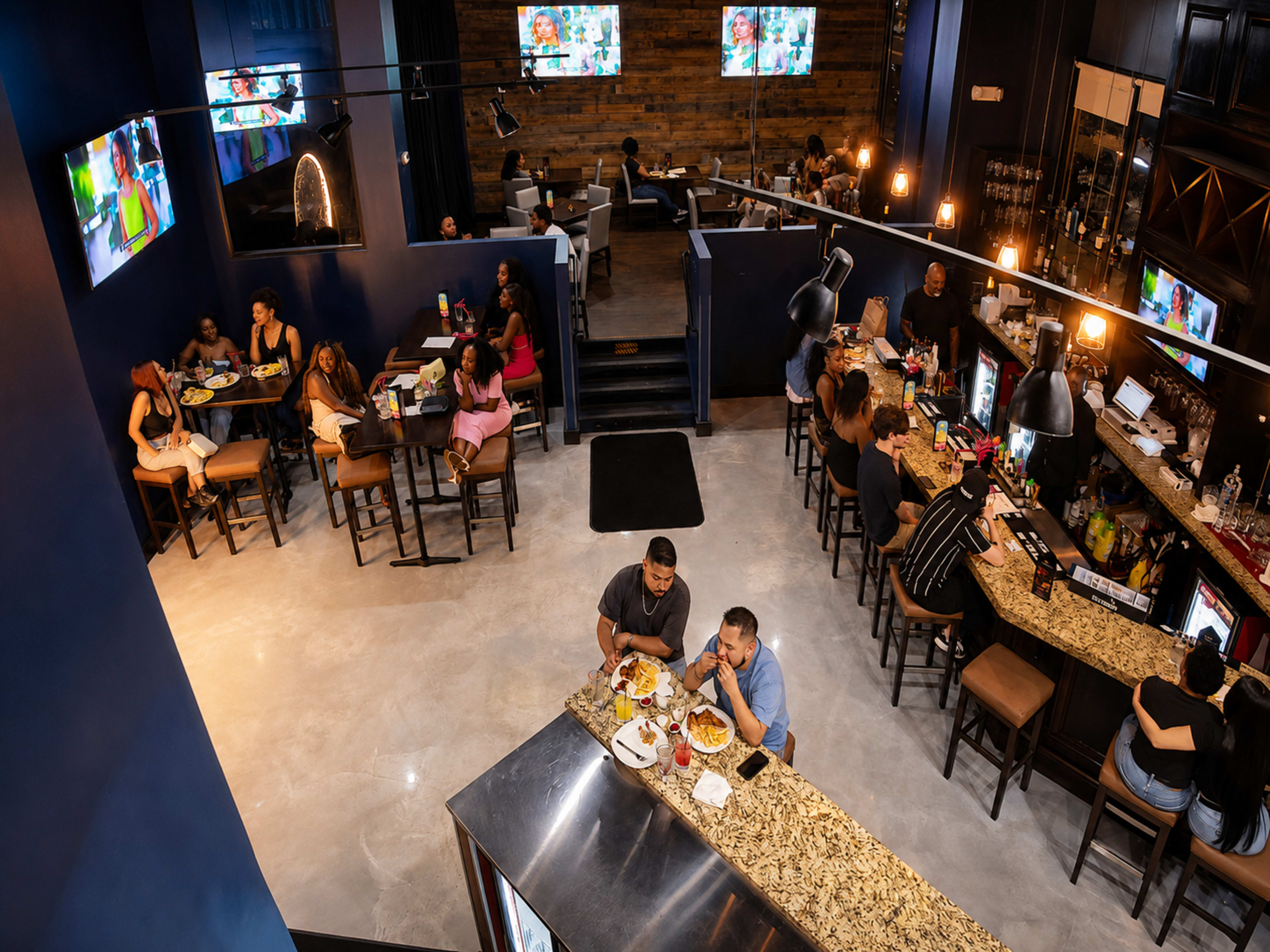 The image shows a vibrant restaurant interior with customers seated at tables and a bar, featuring televisions on the walls and a decorative ambiance.