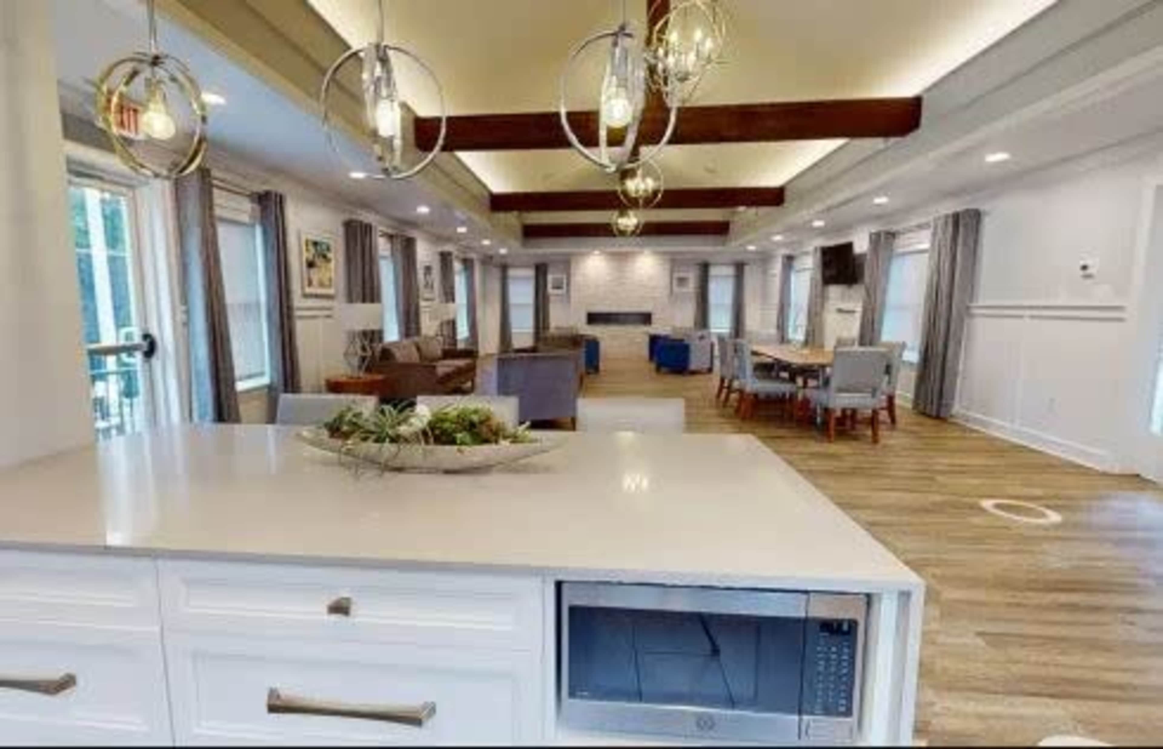 The image shows a modern, open living area with a kitchen counter, comfortable seating, and large windows allowing natural light.
