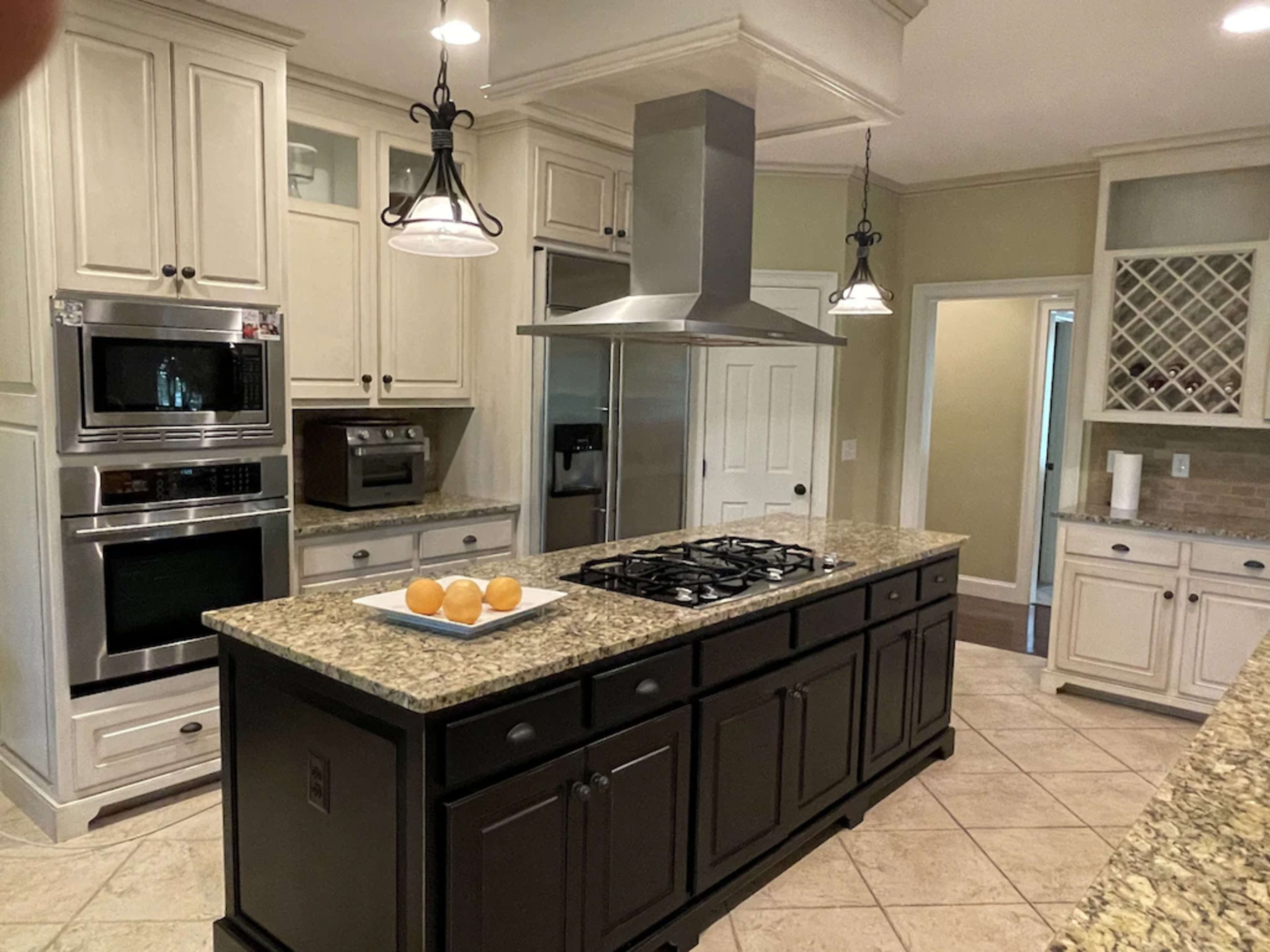 A kitchen features an island with a gas stovetop, flanked by stainless steel appliances and light-colored cabinetry.