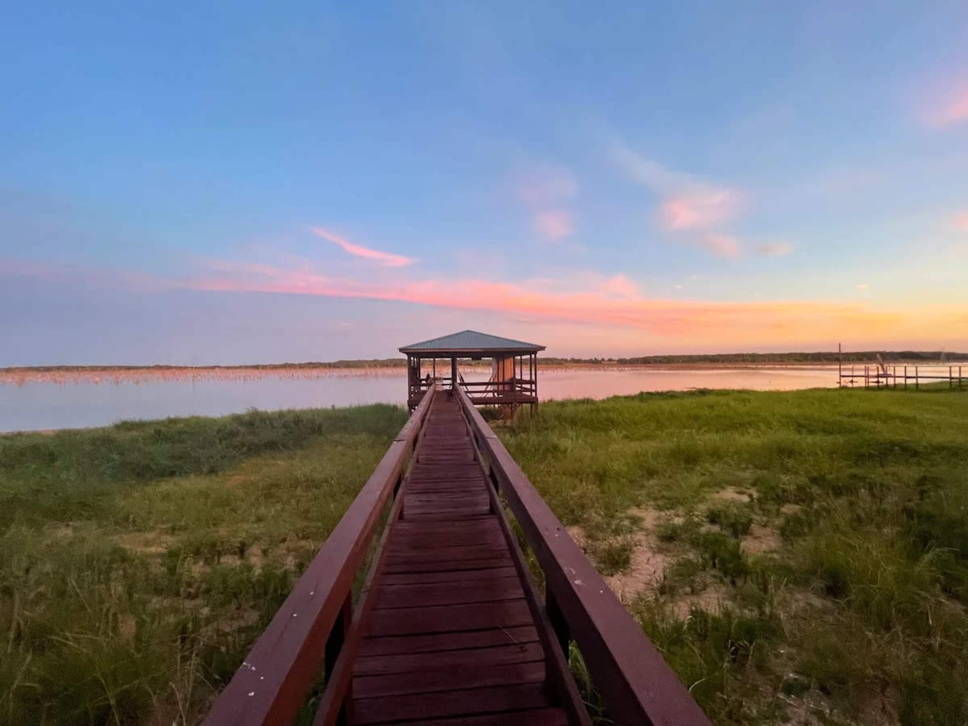A wooden dock extends into a calm body of water beneath a colorful sunset.