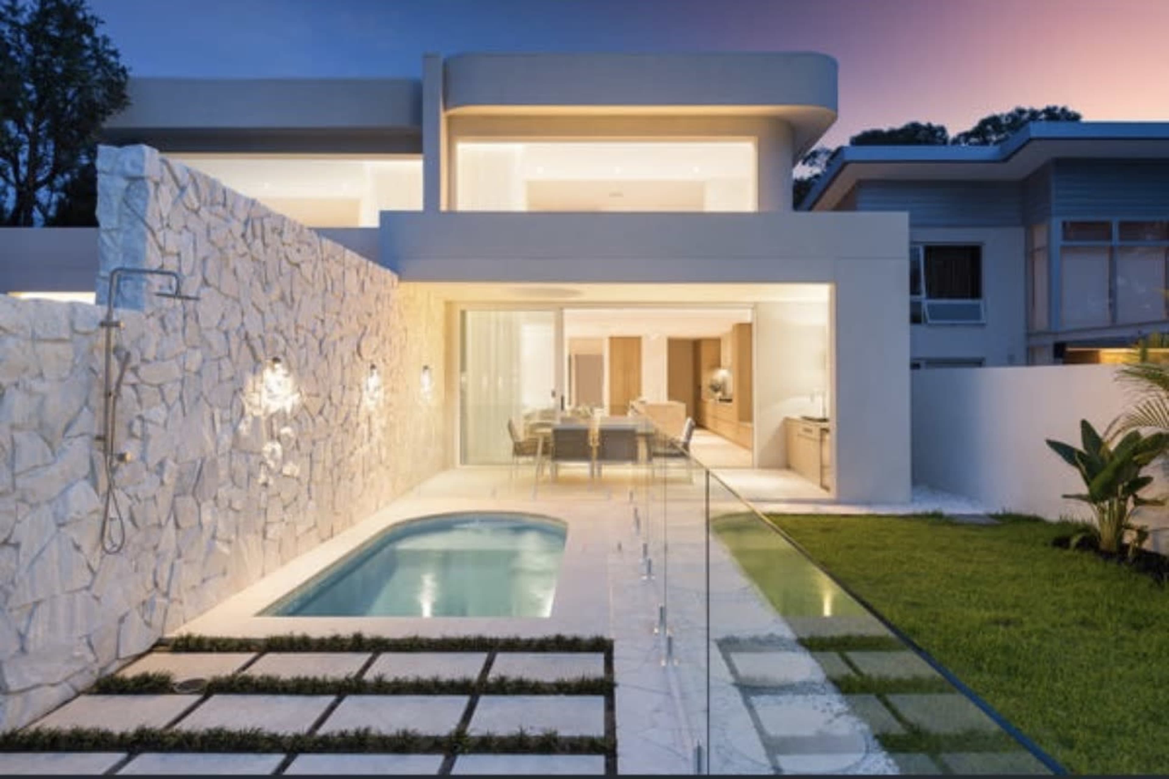 The image shows a modern house with a small swimming pool, surrounded by a meticulously landscaped yard featuring stone pathways and a stone wall.