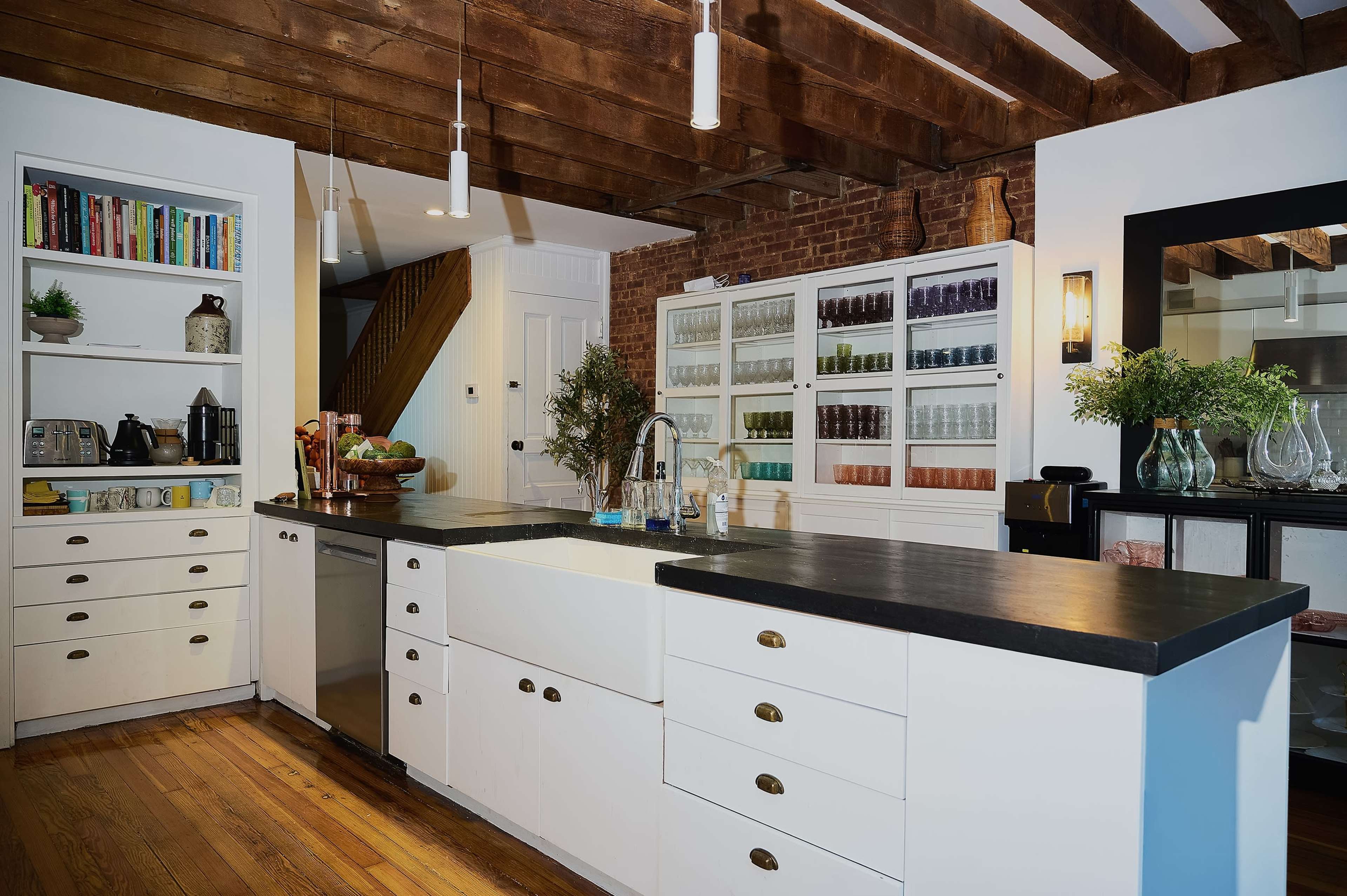 The kitchen features an island with a dark countertop, surrounded by white cabinets and shelves filled with colorful glassware.