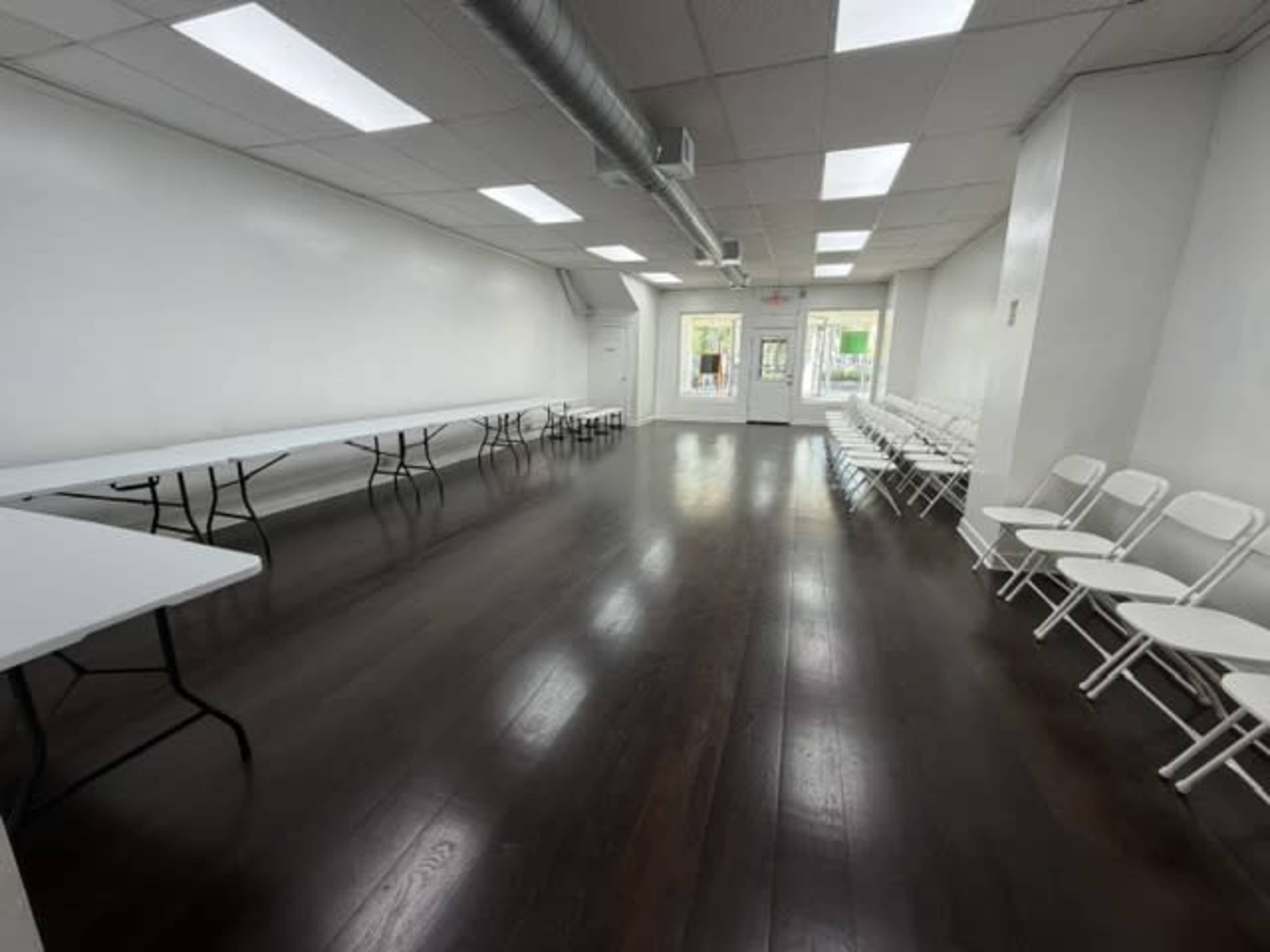 The image shows a large, empty room with several tables arranged in the center and seating along the walls.