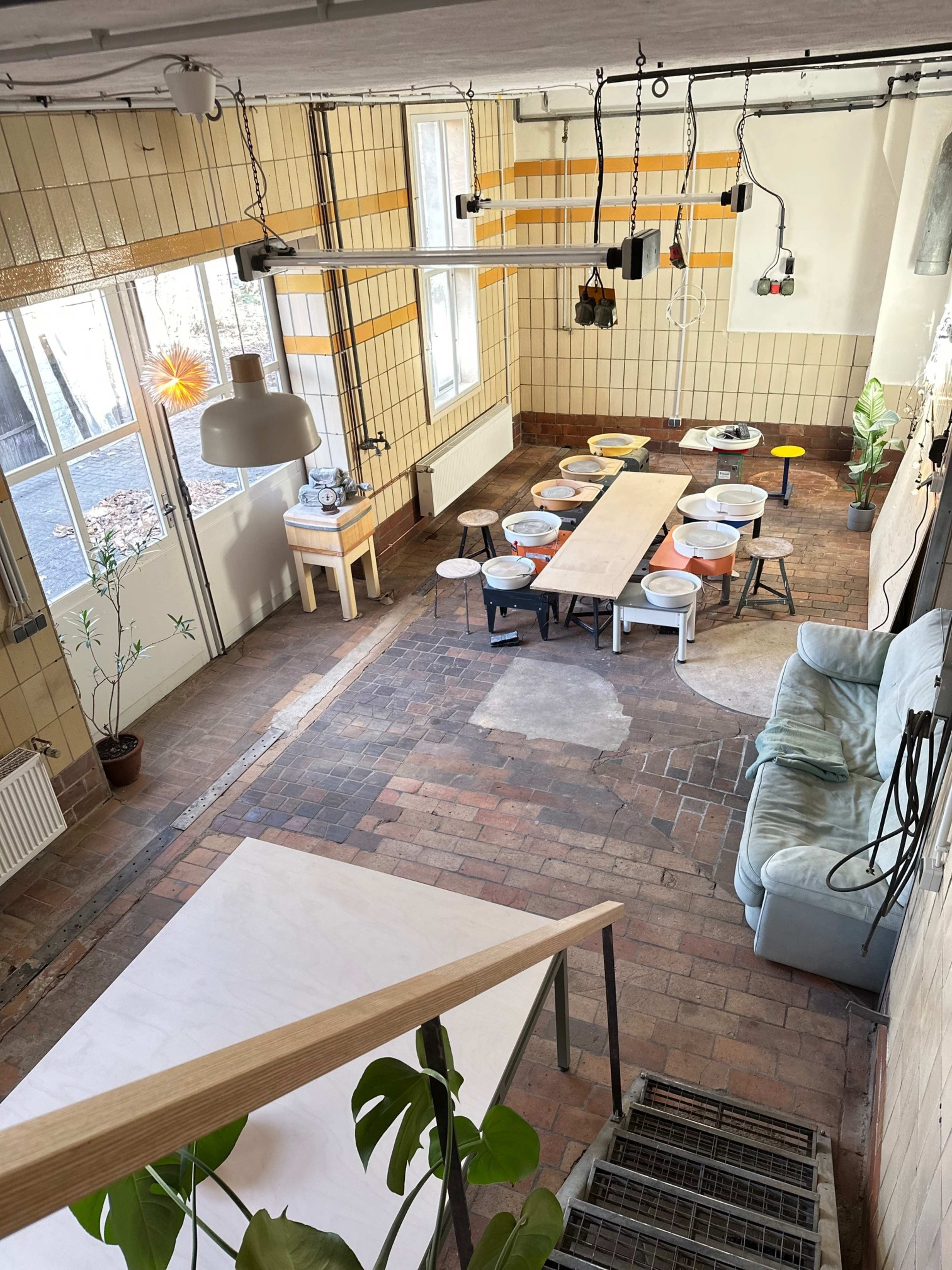 The image shows a spacious, empty room with tiled walls, a long table surrounded by chairs, and a cozy seating area with a sofa.