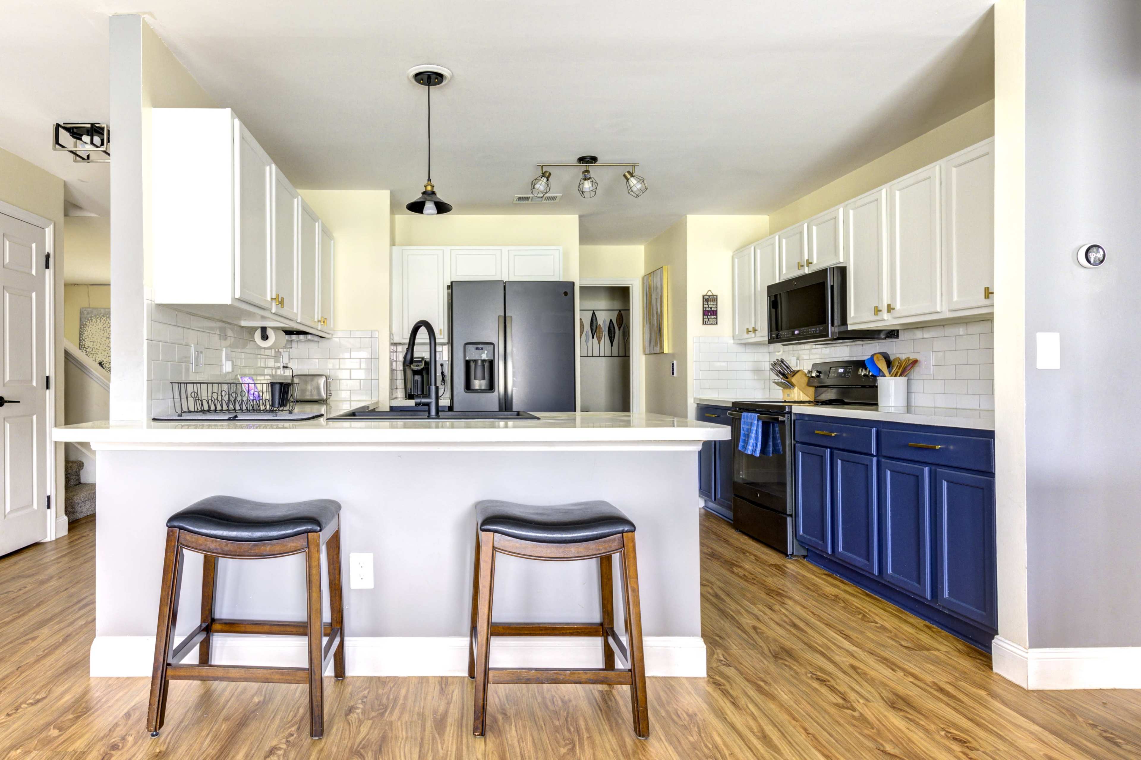 A modern kitchen features white and blue cabinetry, stainless steel appliances, and a breakfast bar with two stools.
