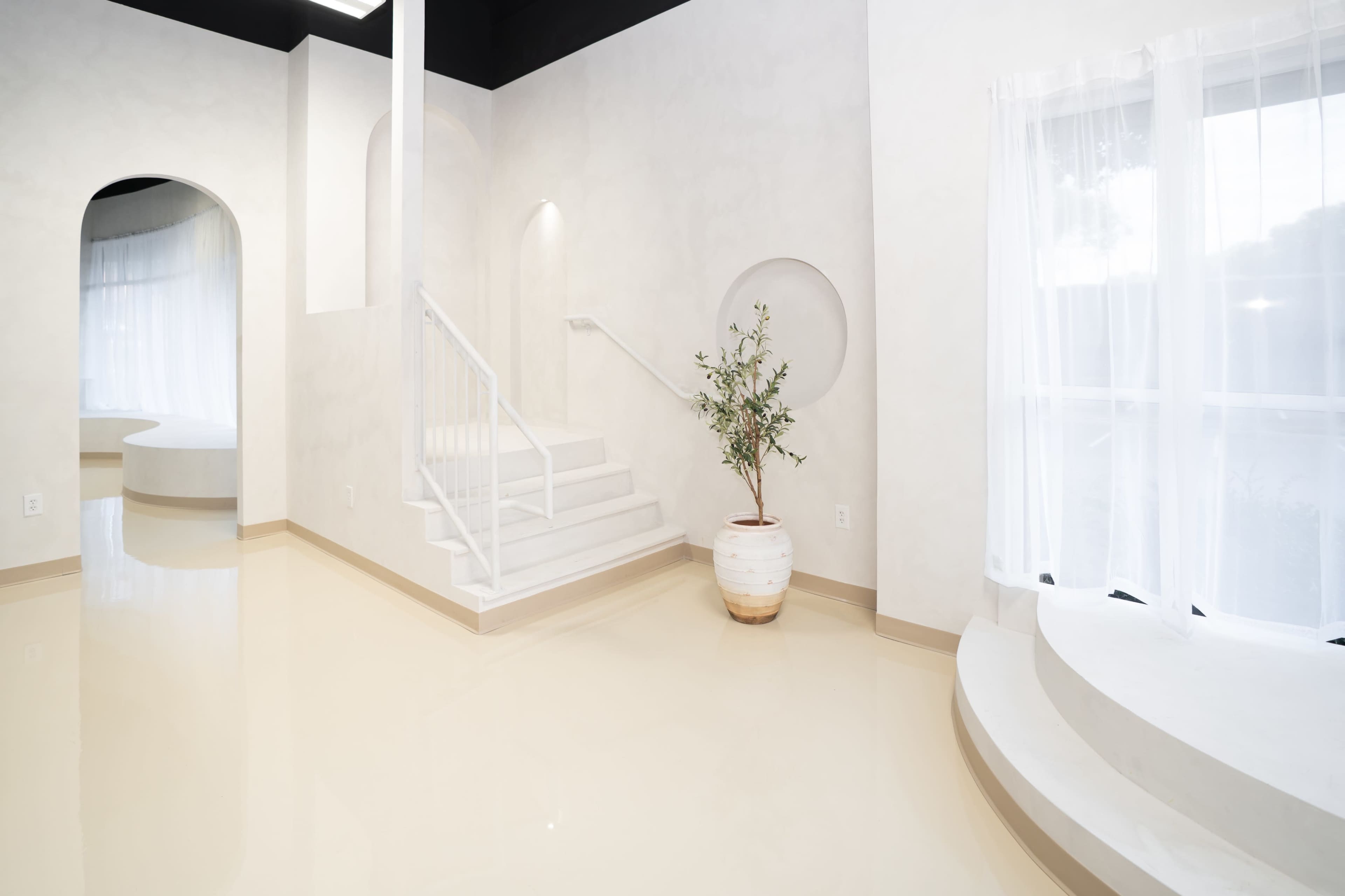 The interior features a bright, minimalist design with curved walls, a staircase, and a potted plant.