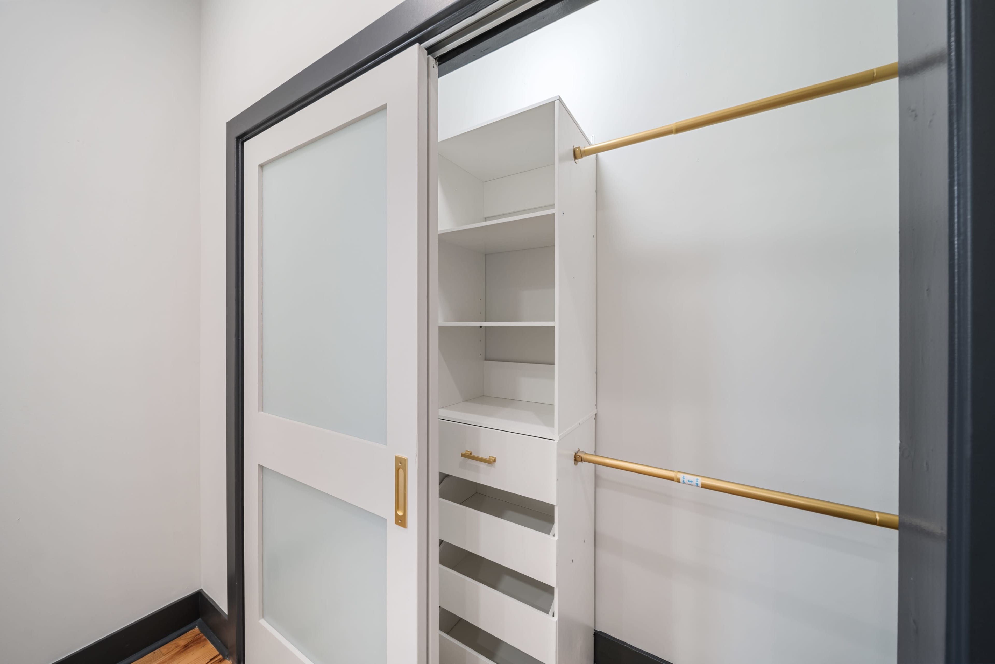 The image shows a minimalist closet with a sliding door, open shelving, and a hanging rod for clothes.