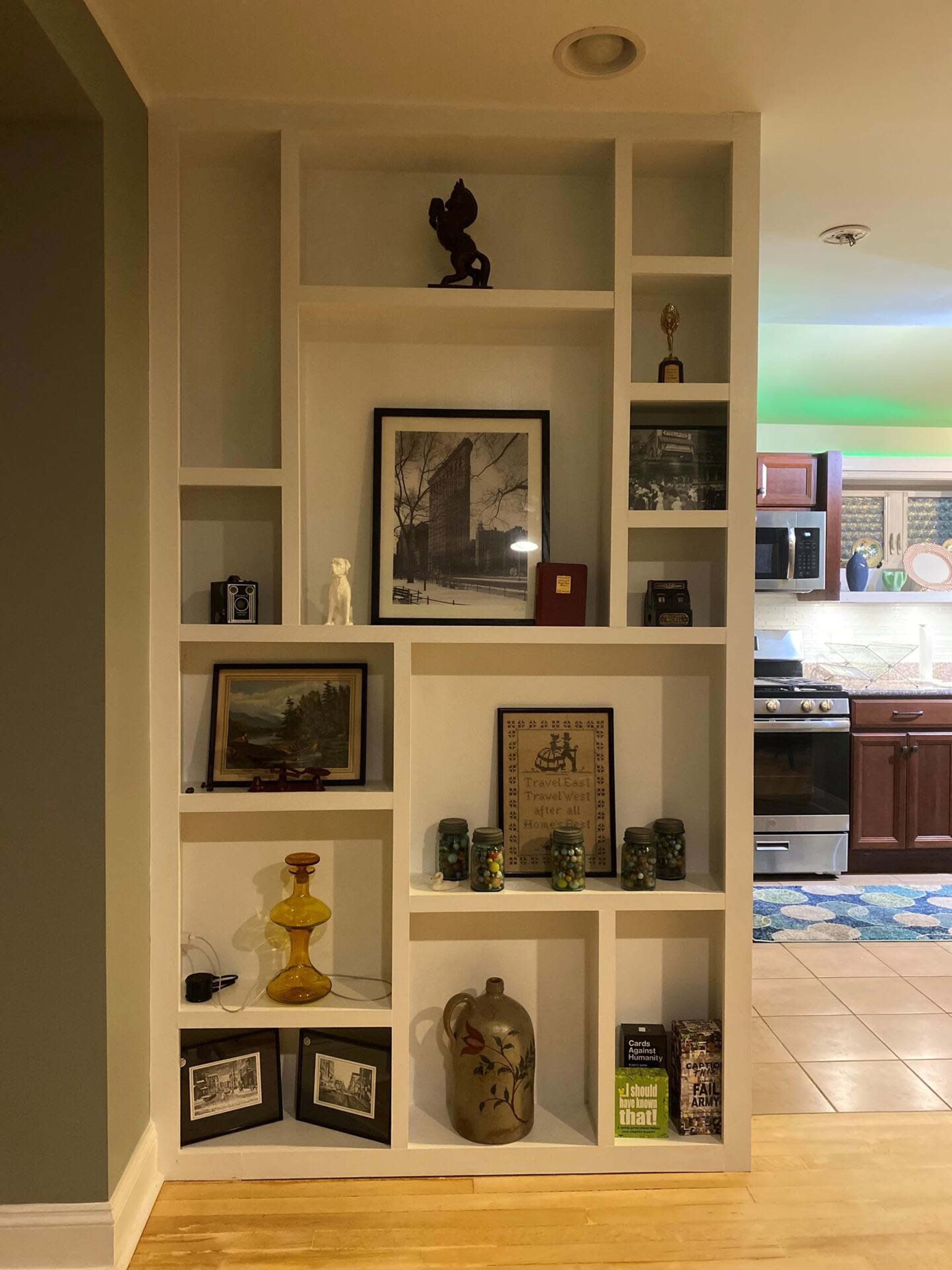 A white shelving unit filled with various decorative items, including framed photographs, a small statue, a trophy, and glass jars.