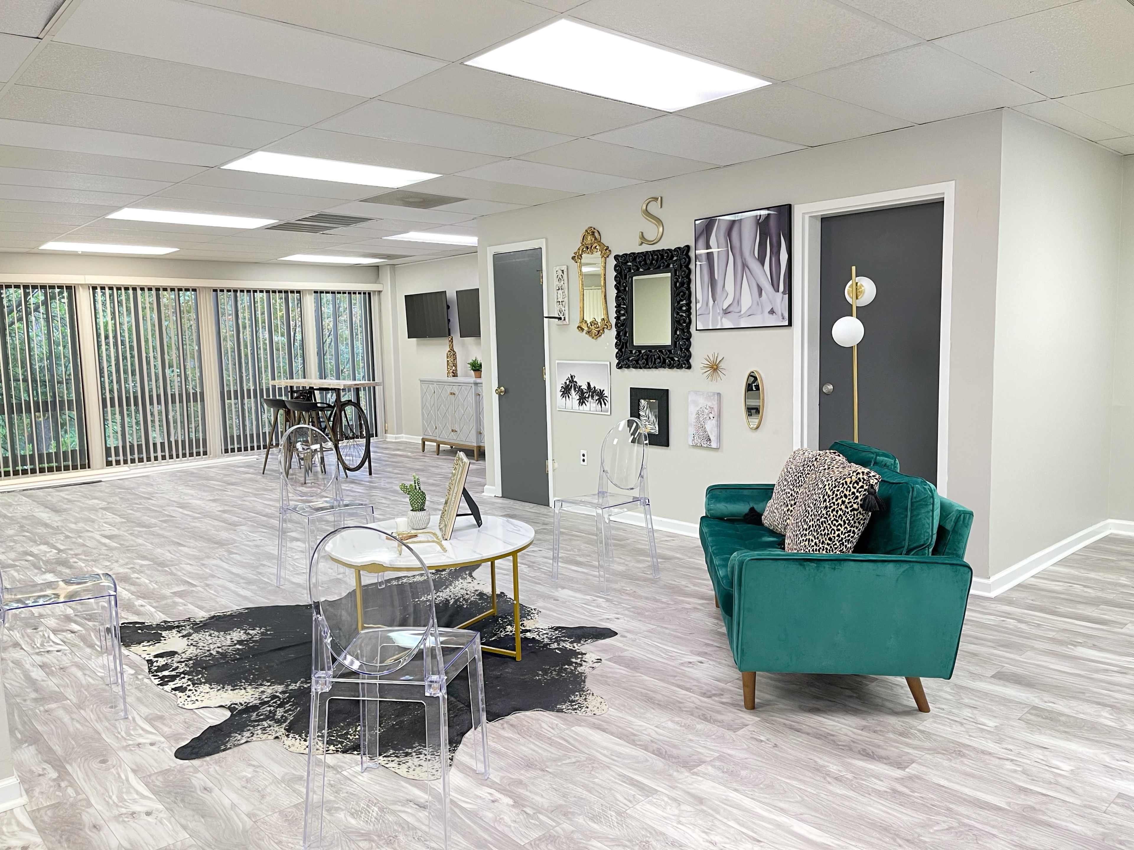 A spacious, modern interior features a green velvet couch, a clear acrylic coffee table, and various artworks displayed on the walls.