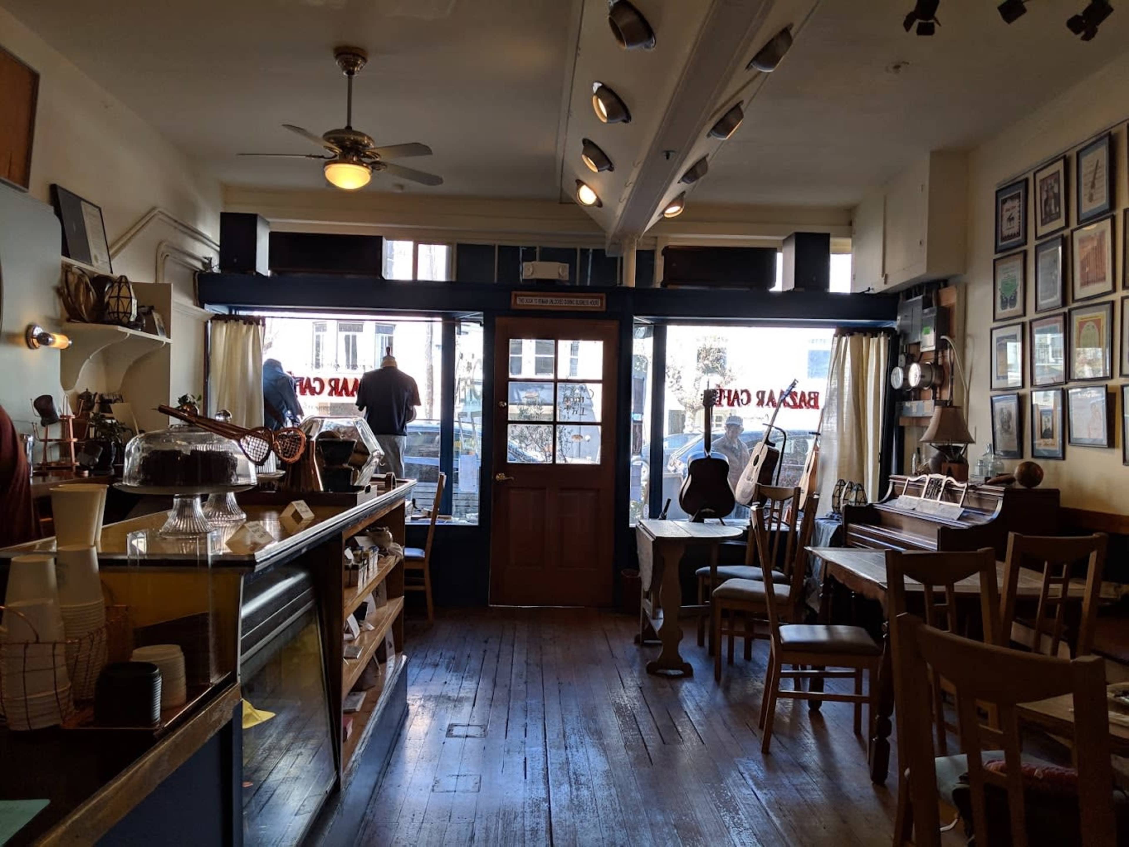 A cozy café interior features a wooden counter, scattered tables, and large windows displaying a street view.