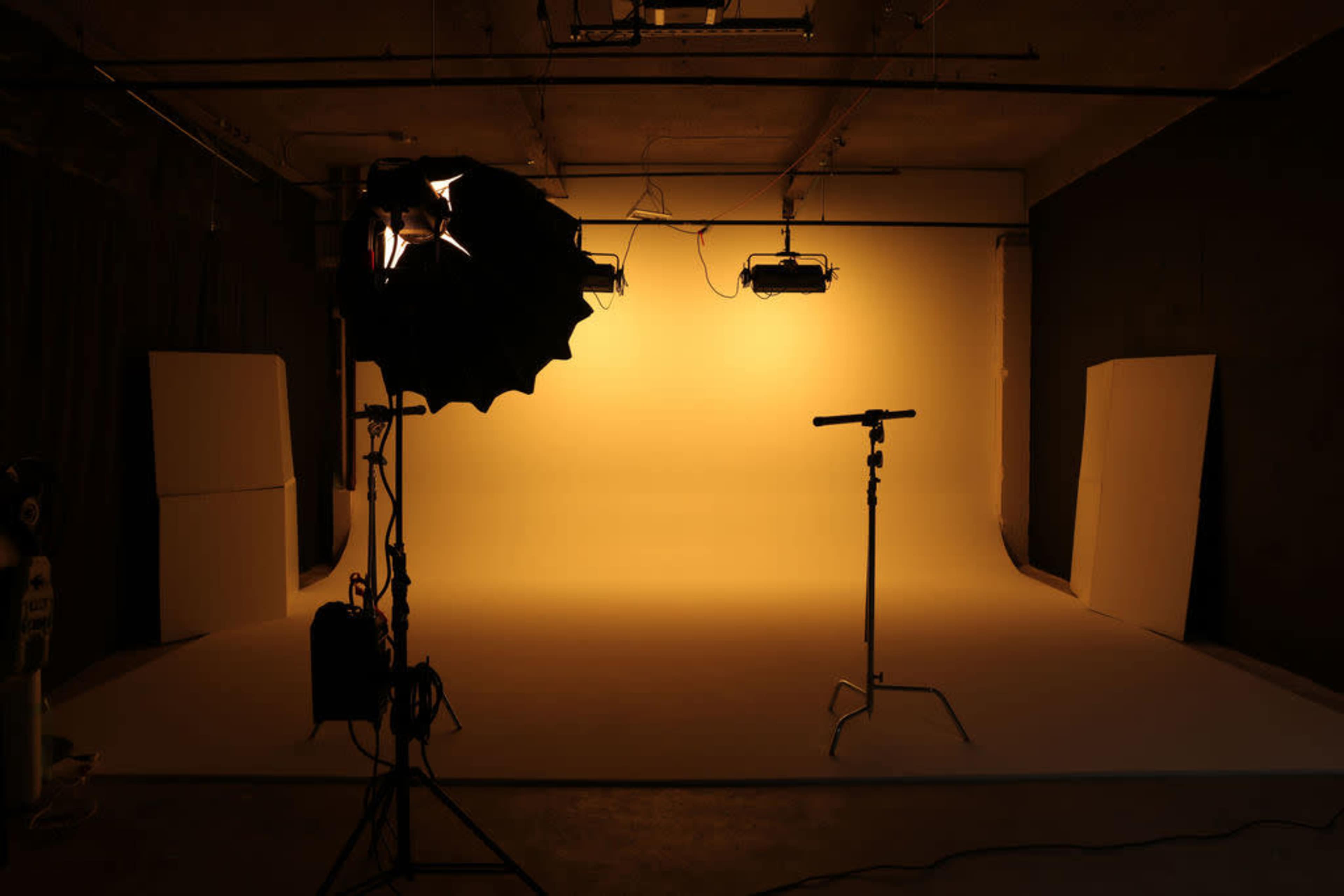 The image shows a photography studio with a yellow background, lighting setup, and a backdrop stand.