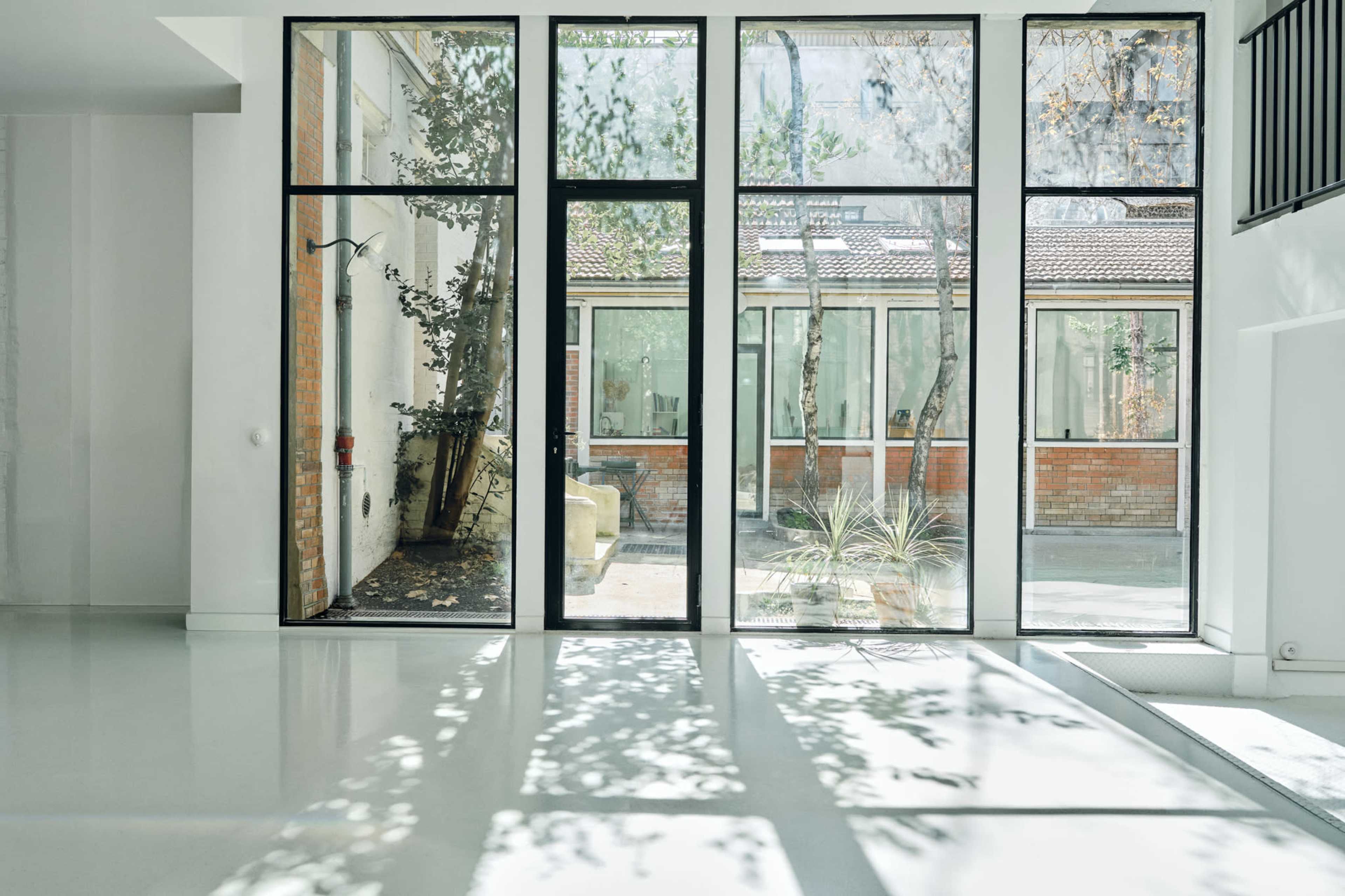 The image features a modern interior space with large glass windows revealing a landscaped outdoor courtyard filled with trees and natural light.