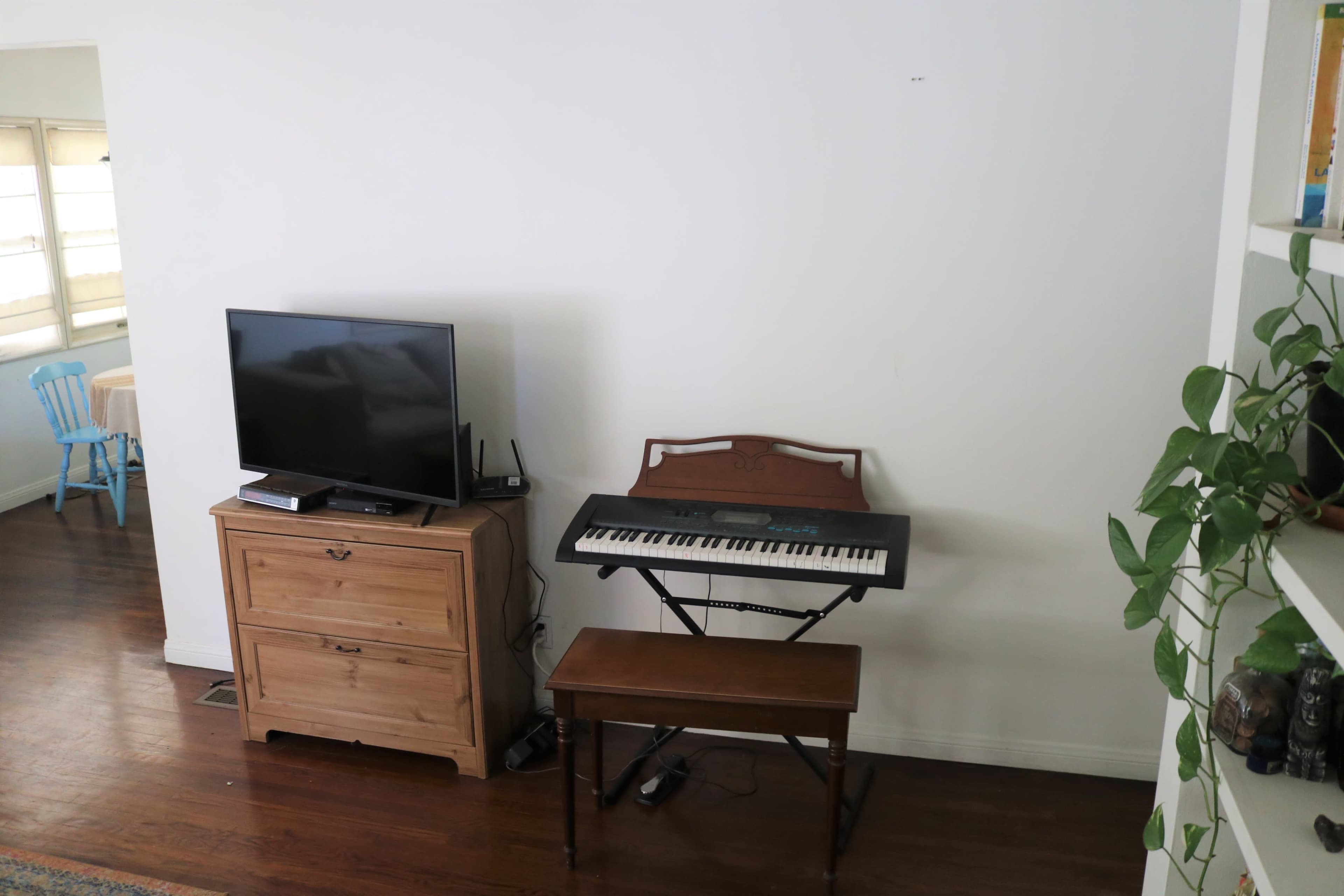 A small room with a television on a wooden dresser next to a keyboard on a stand, accompanied by a bench.