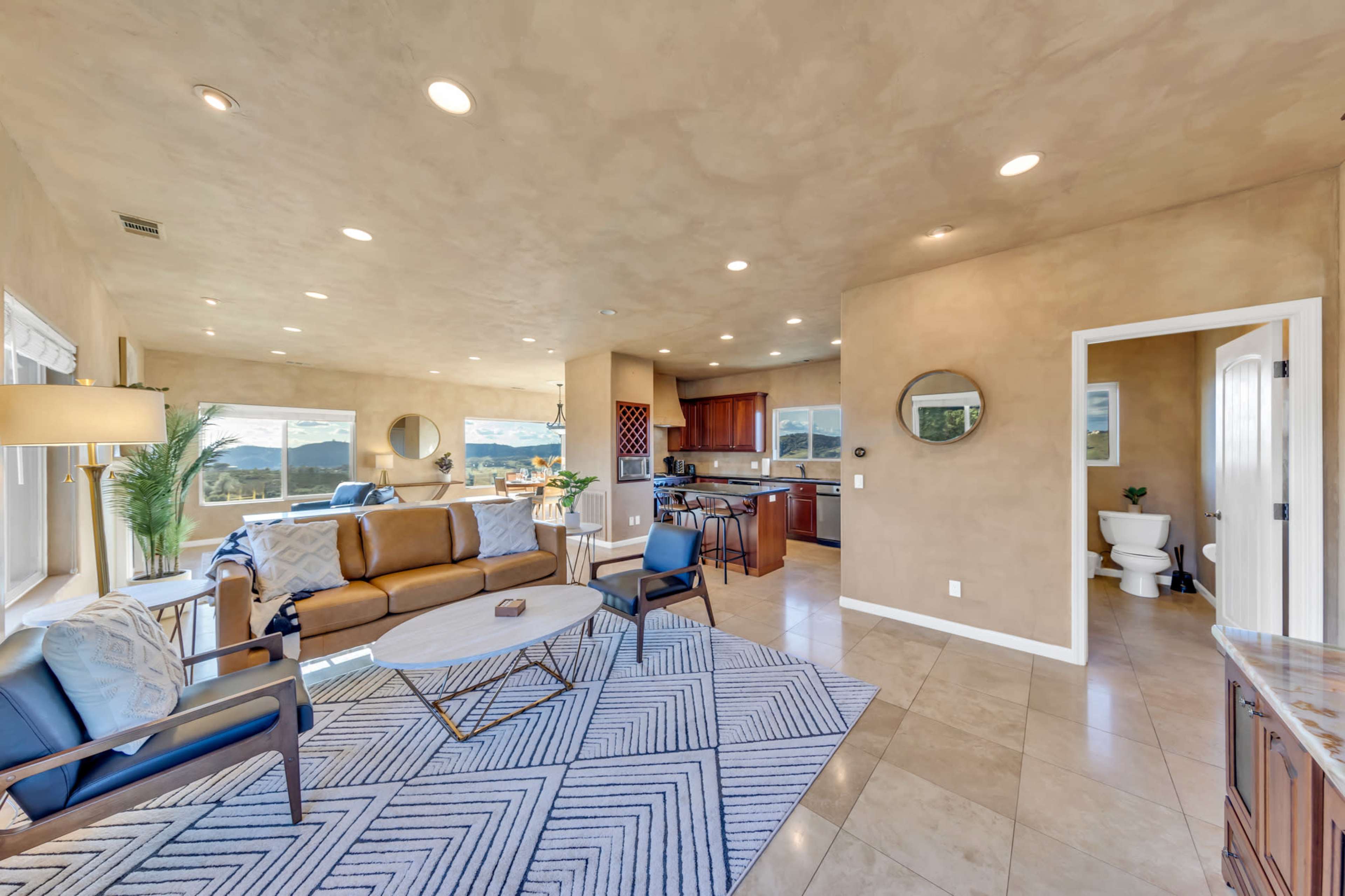 A modern living room with a beige color palette, featuring a sectional sofa, a coffee table, and an open view into a kitchen area.