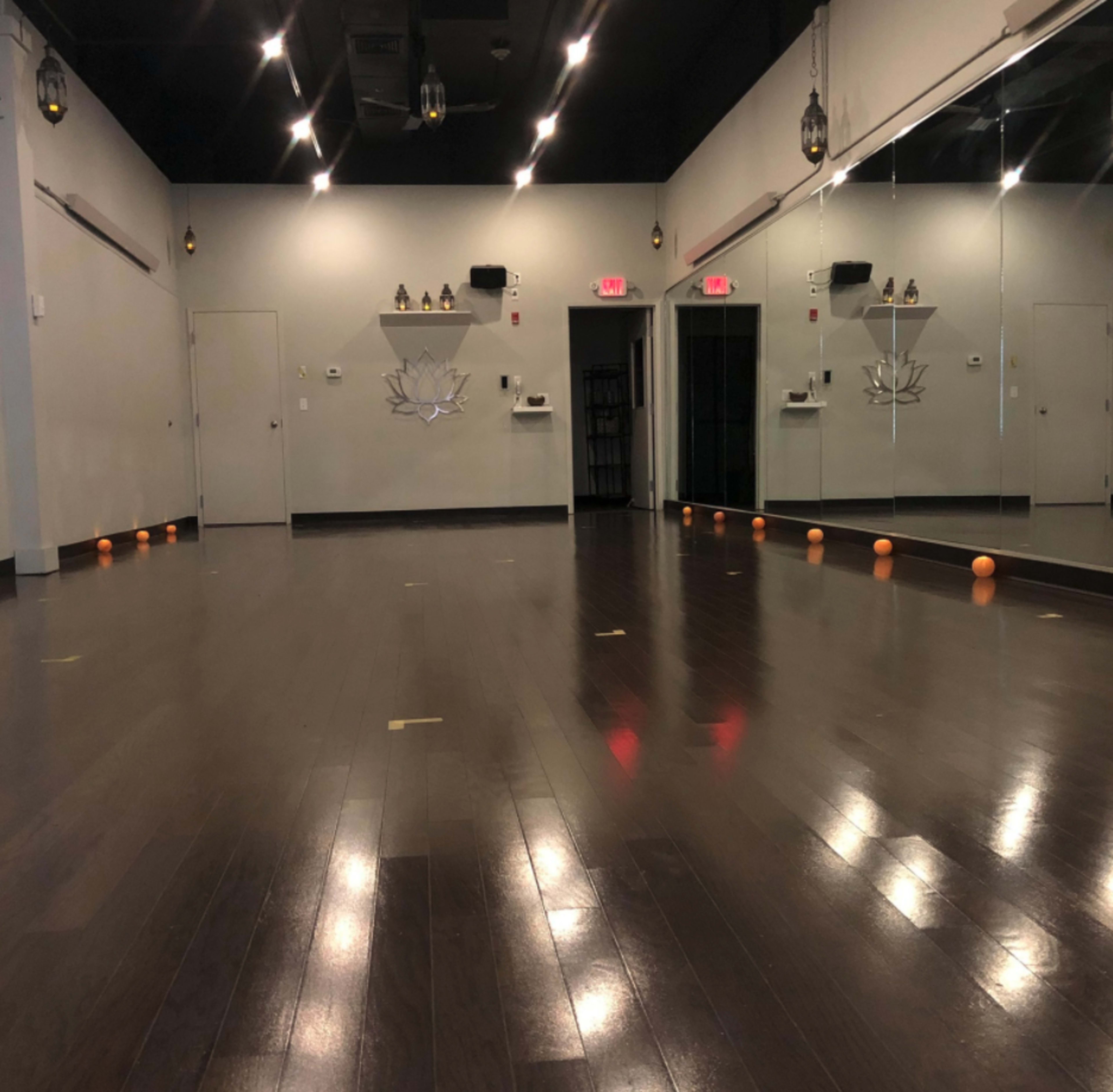 An empty studio with polished wooden floors, mirrors on one wall, and several small orange objects lined up along the floor.