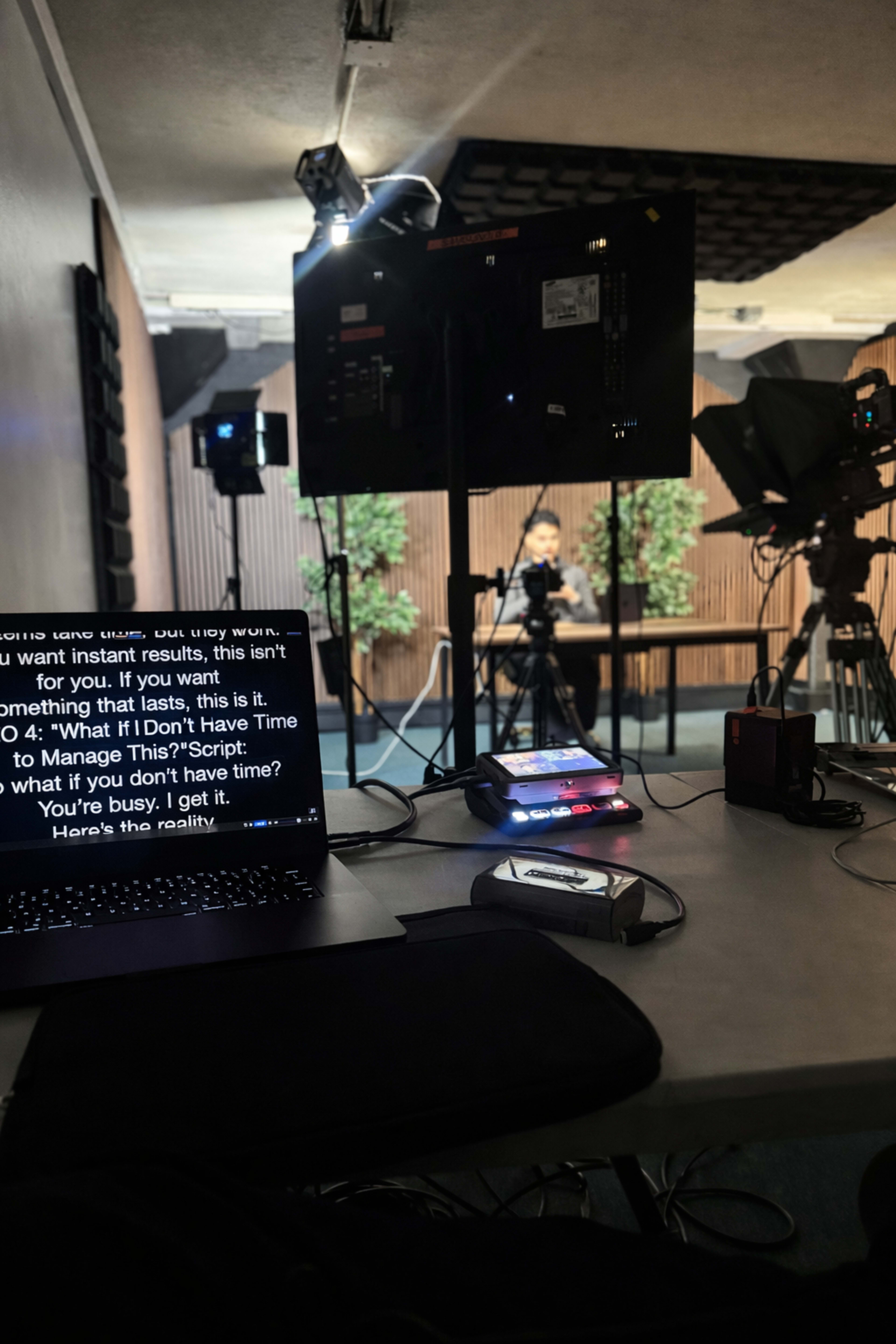 A production setup features a laptop displaying a script on teleprompter software, with cameras and a set arranged for recording in the background.