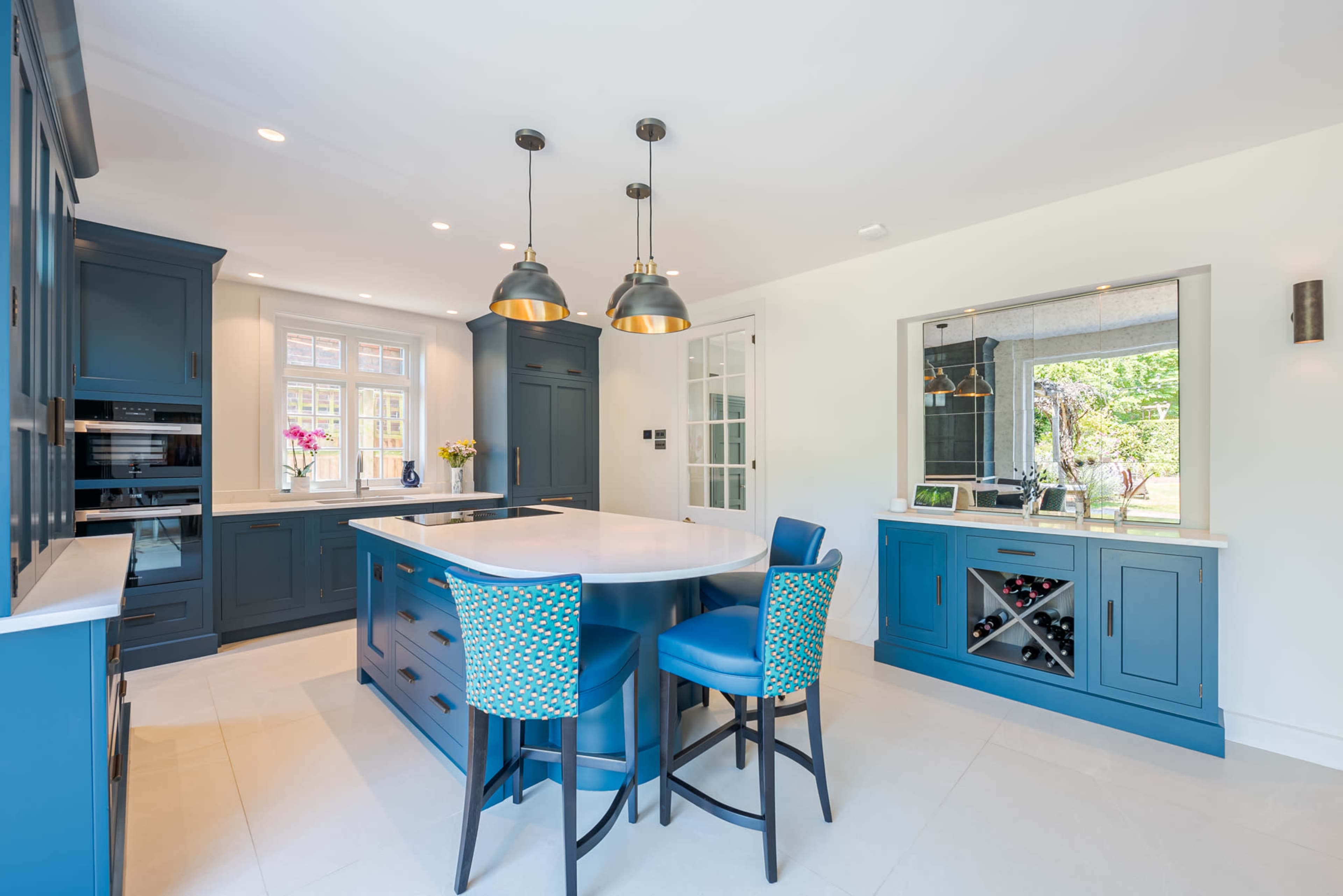 A modern kitchen features blue cabinetry, a large island with a white countertop, and two blue barstools, illuminated by pendant lights.
