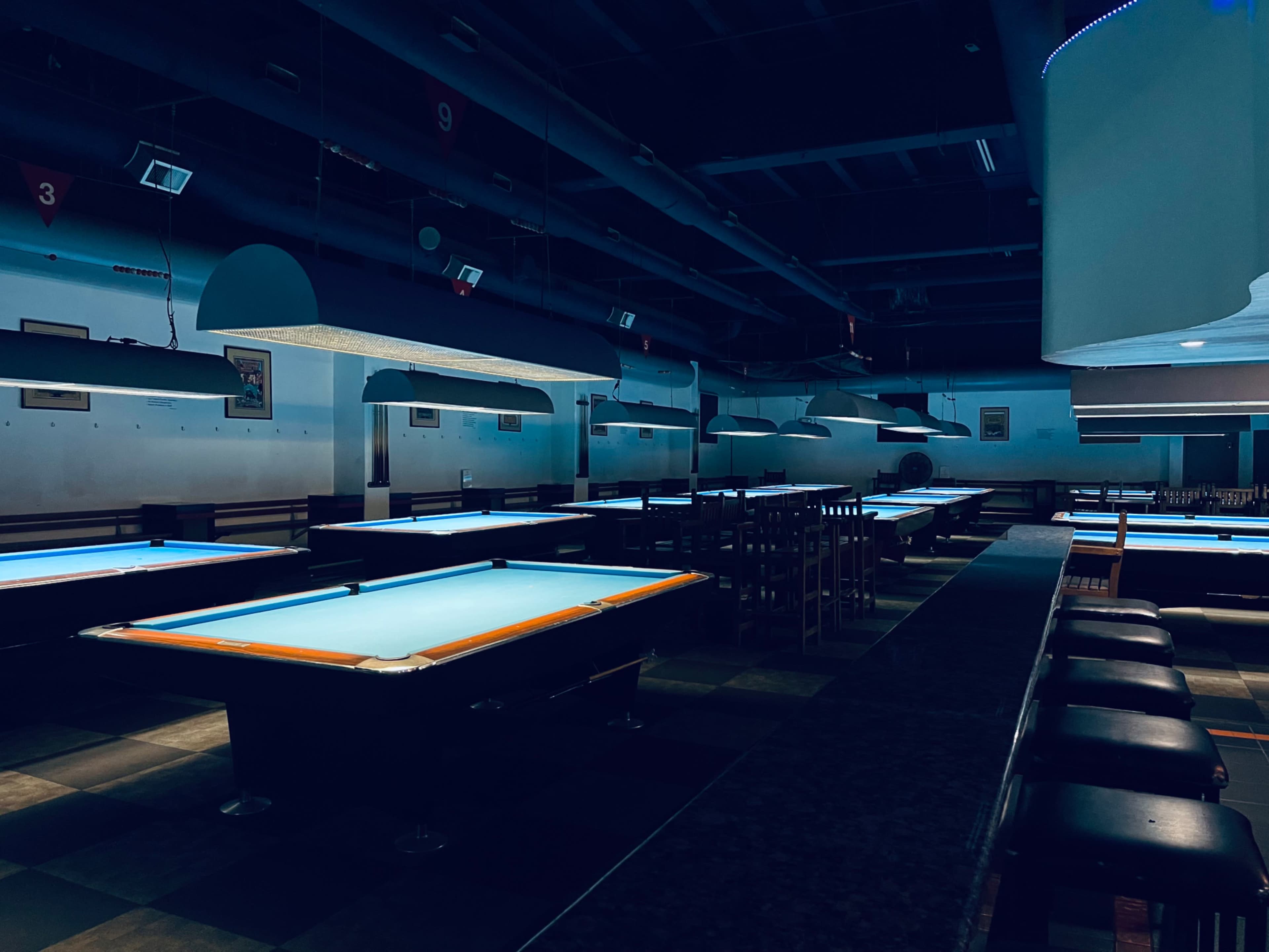 An empty billiards hall features several pool tables illuminated by overhead lights.
