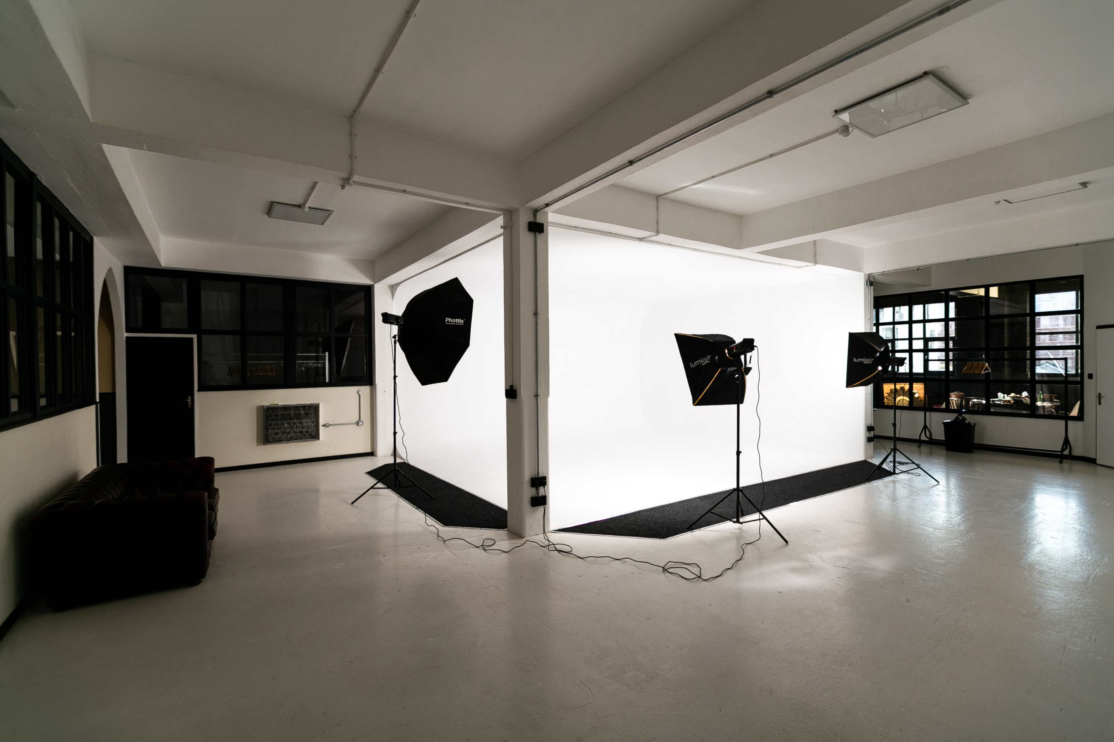 A photography studio features a seamless white backdrop illuminated by several softbox lights and has a minimalist design.