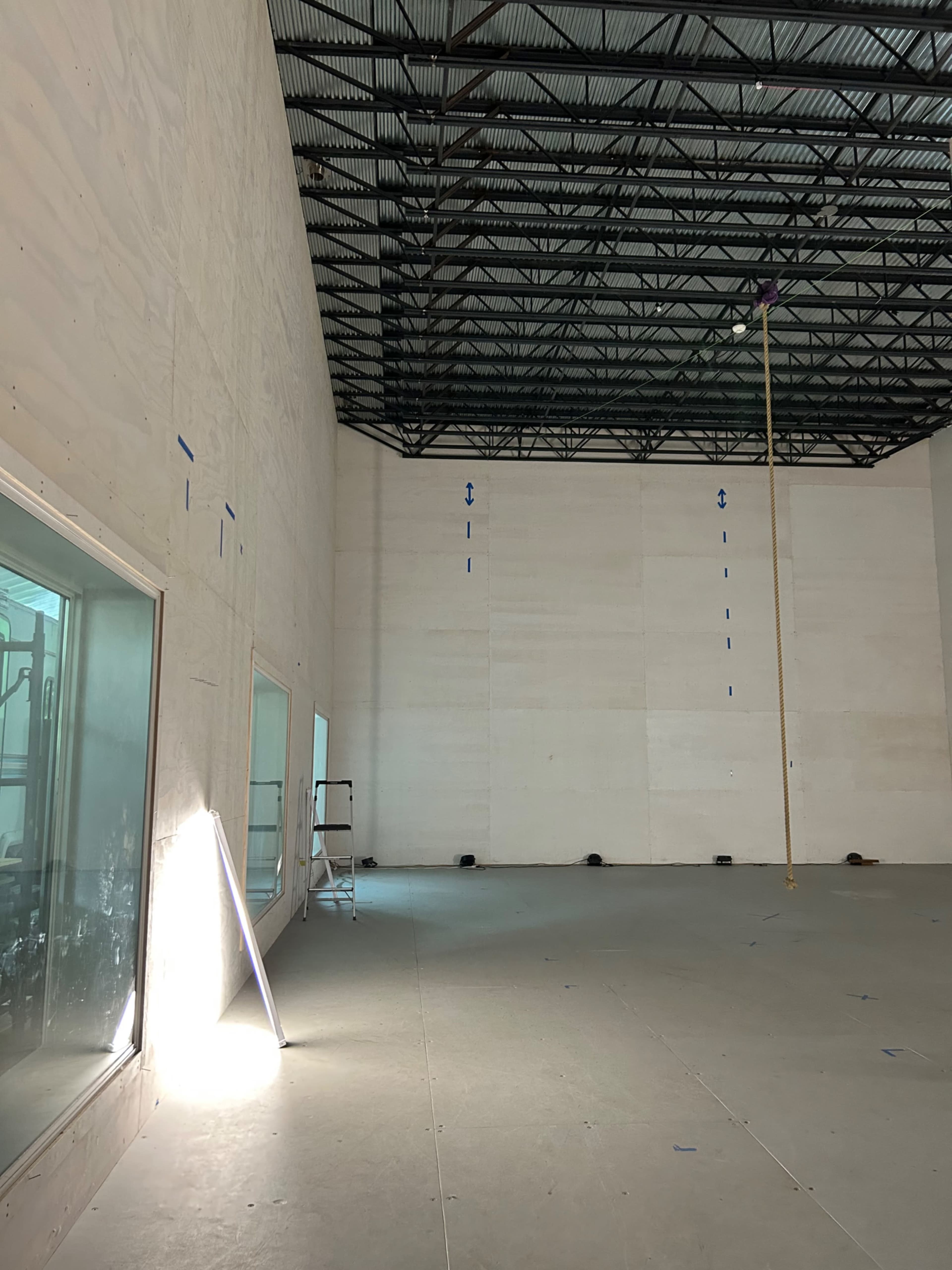 A spacious interior of a bare building under construction, featuring high ceilings and large windows.