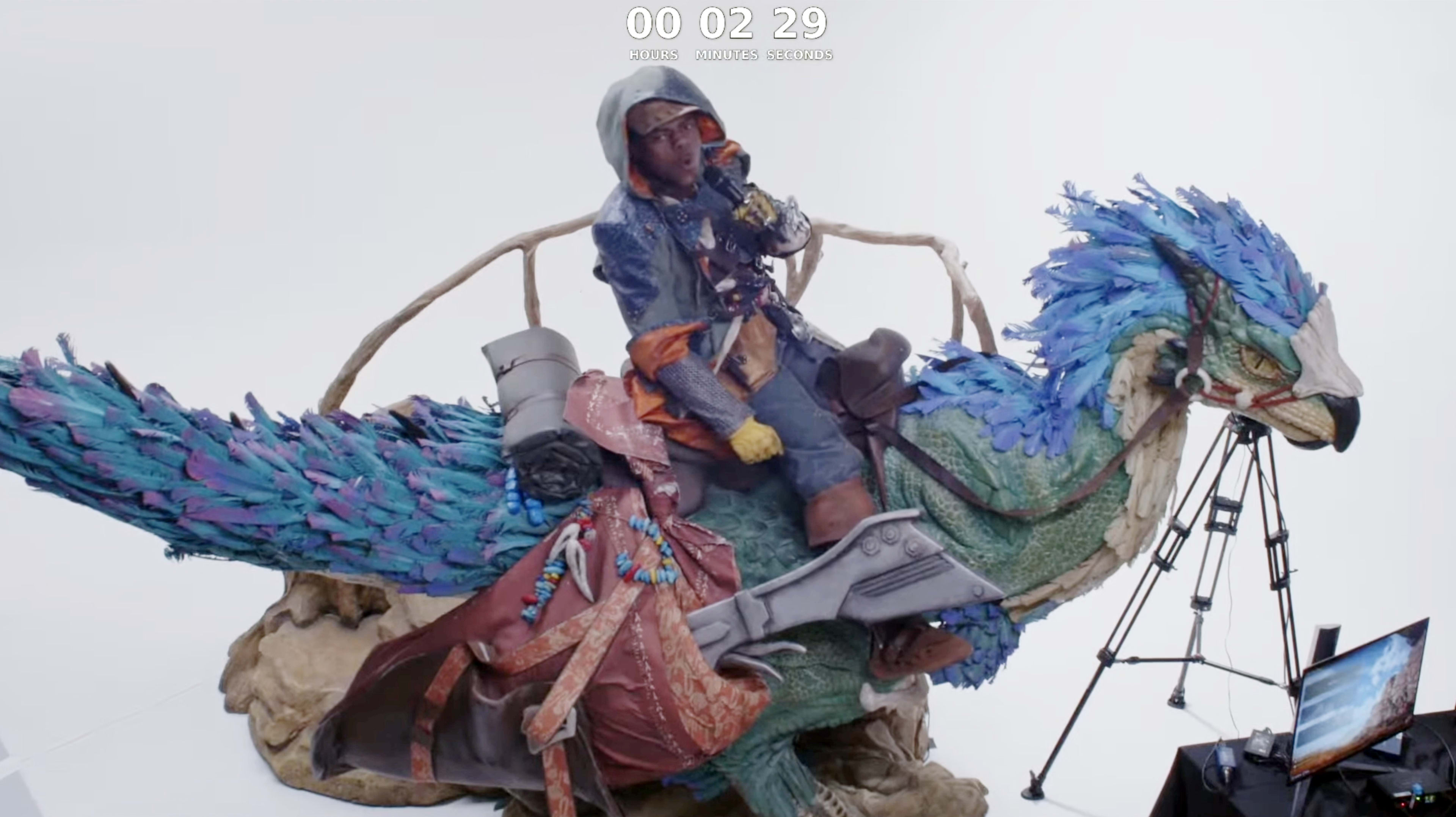 A person dressed in colorful attire sits atop a large, intricately detailed bird statue in a studio setting, with cameras set up nearby.