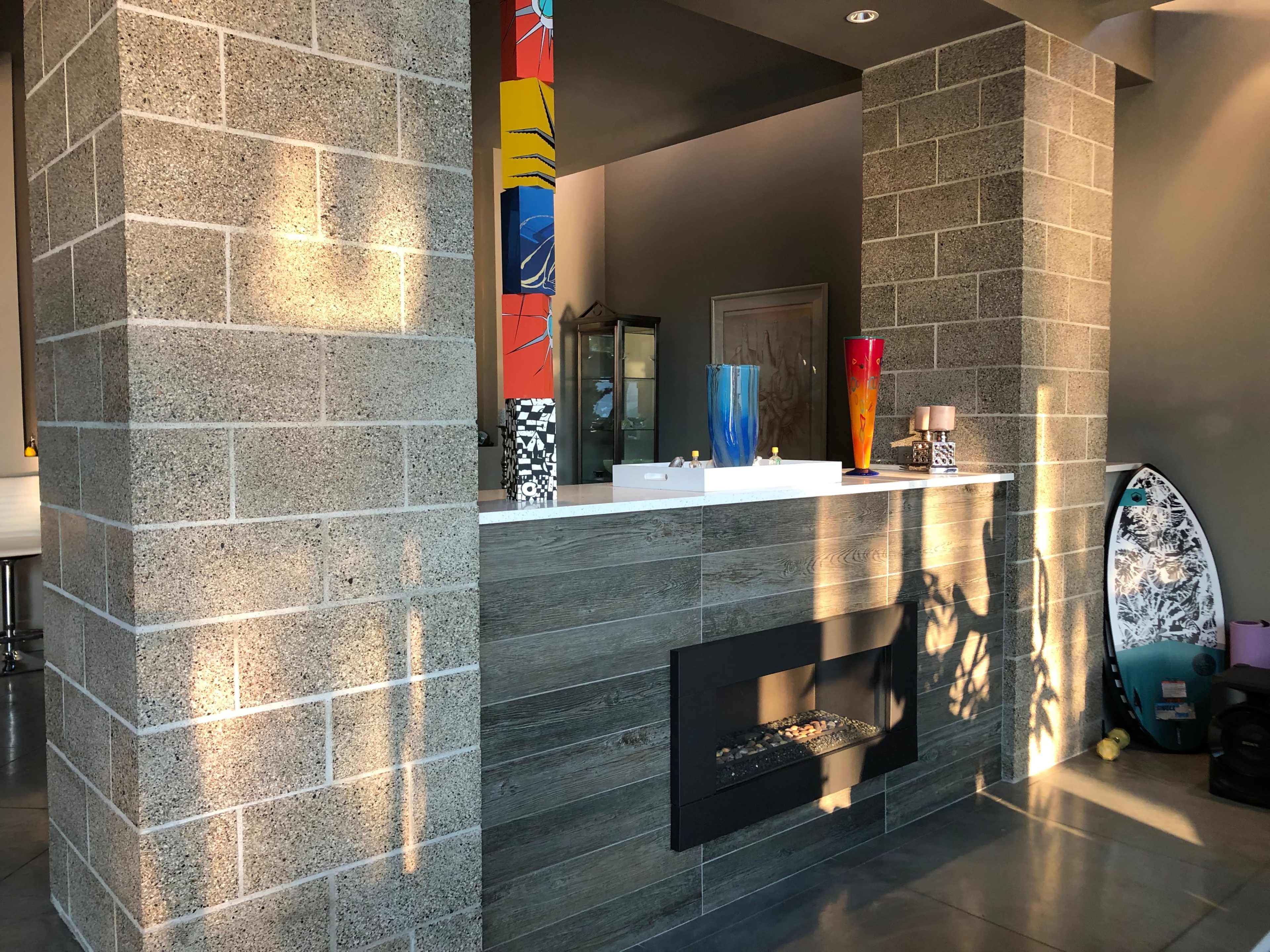 A modern interior with a stylish fireplace, colorful vases, and a surfboard leaning against a wall.