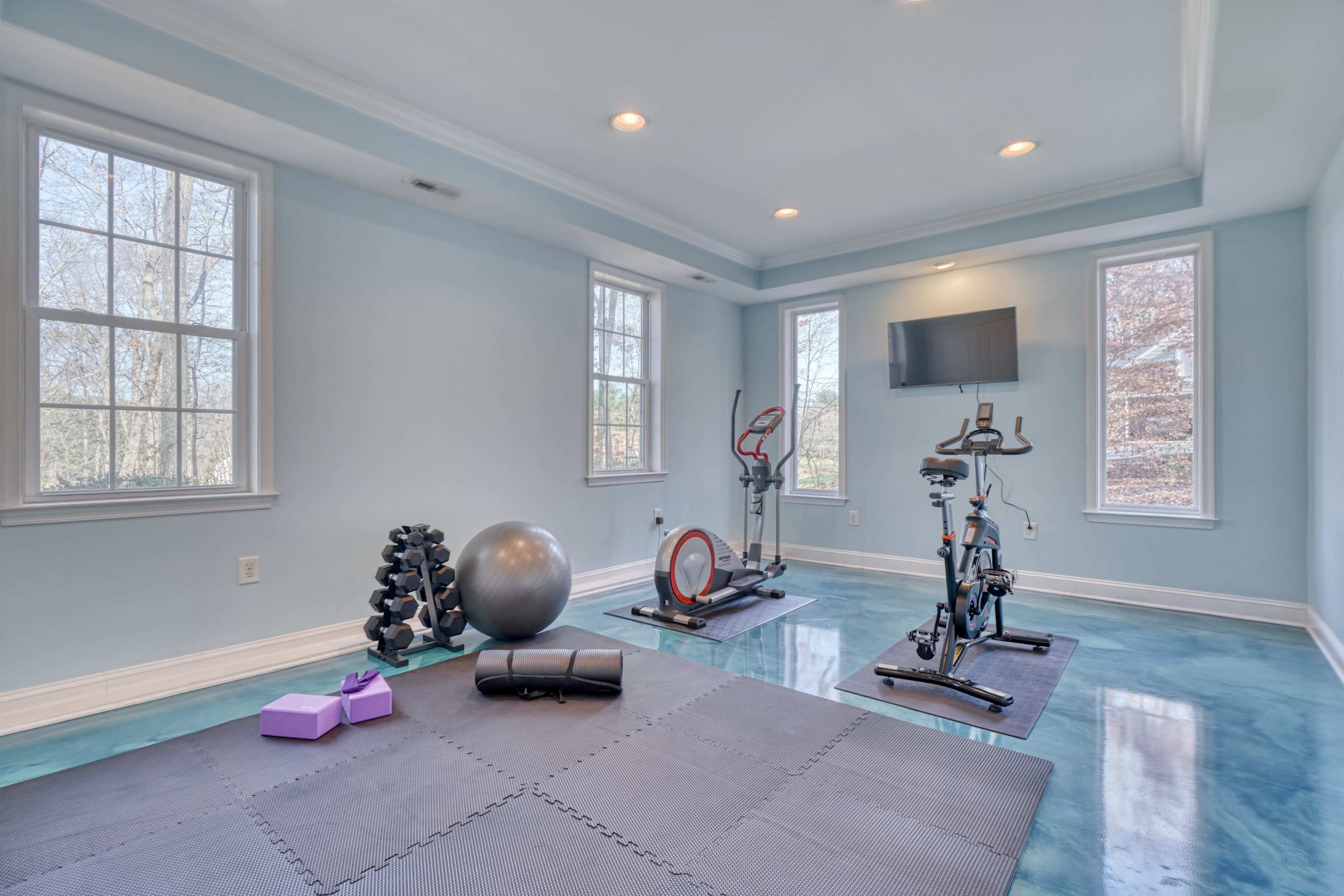 A well-lit home gym featuring exercise equipment, including a stationary bike, a set of weights, and a yoga ball, along with an exercise mat on the floor.
