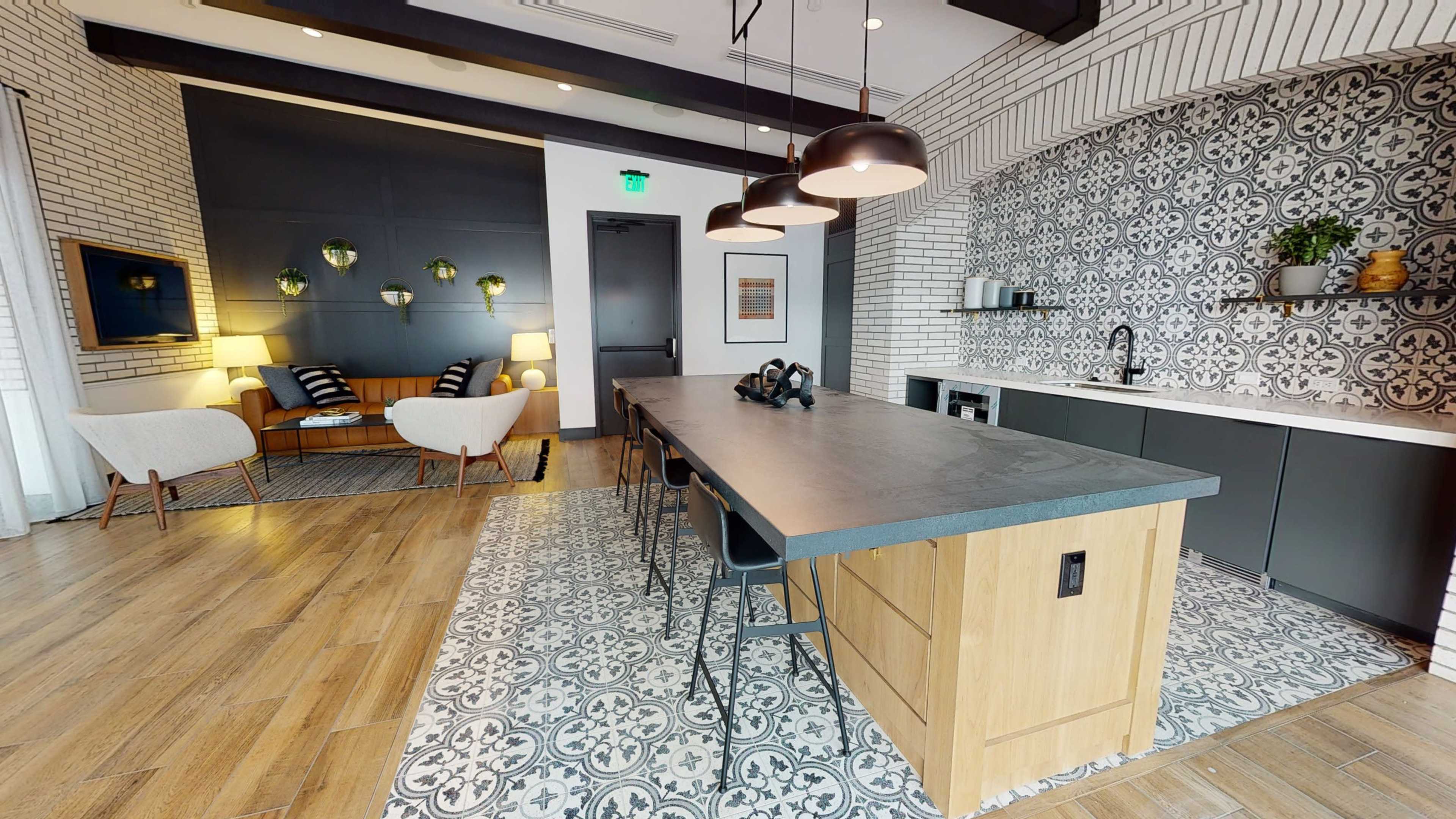 A modern kitchen and living area featuring a large, flat island with bar stools, patterned tile flooring, and a seating arrangement with two armchairs and a sofa.