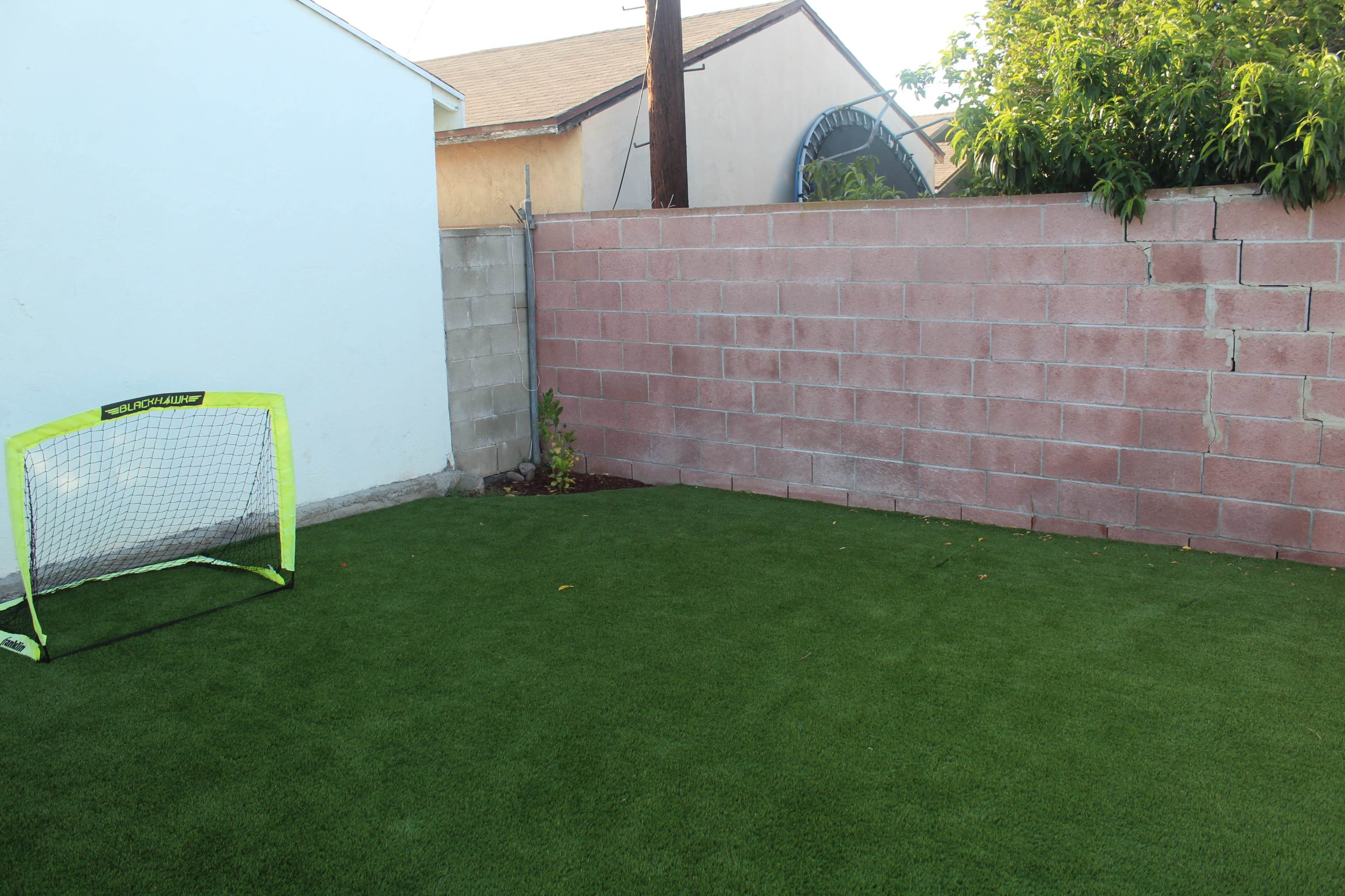 A small backyard with artificial grass and a soccer goal placed against a blank wall.