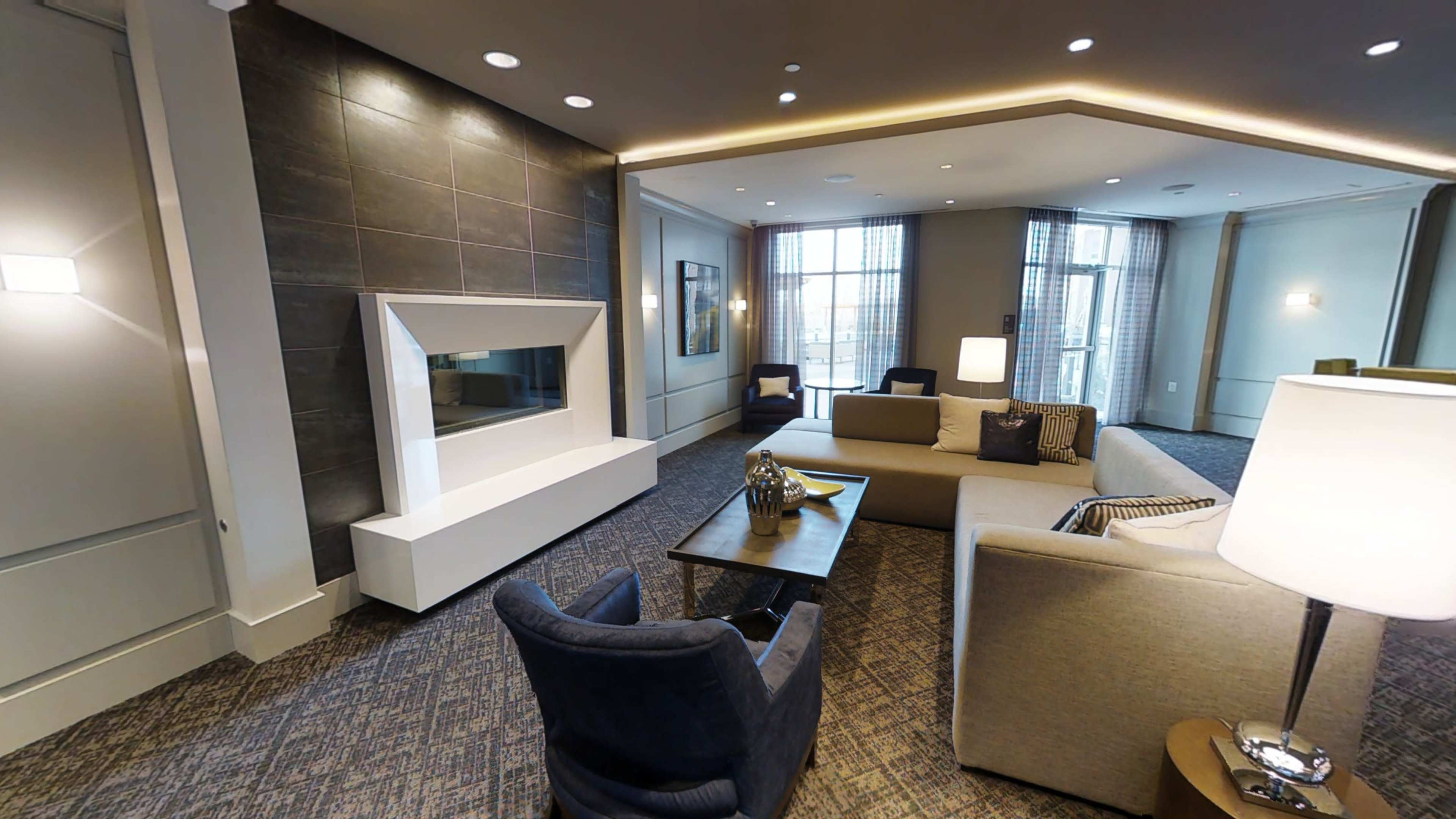 A modern living area features a stylish fireplace, two sofas, a coffee table, and a lamp under soft lighting.