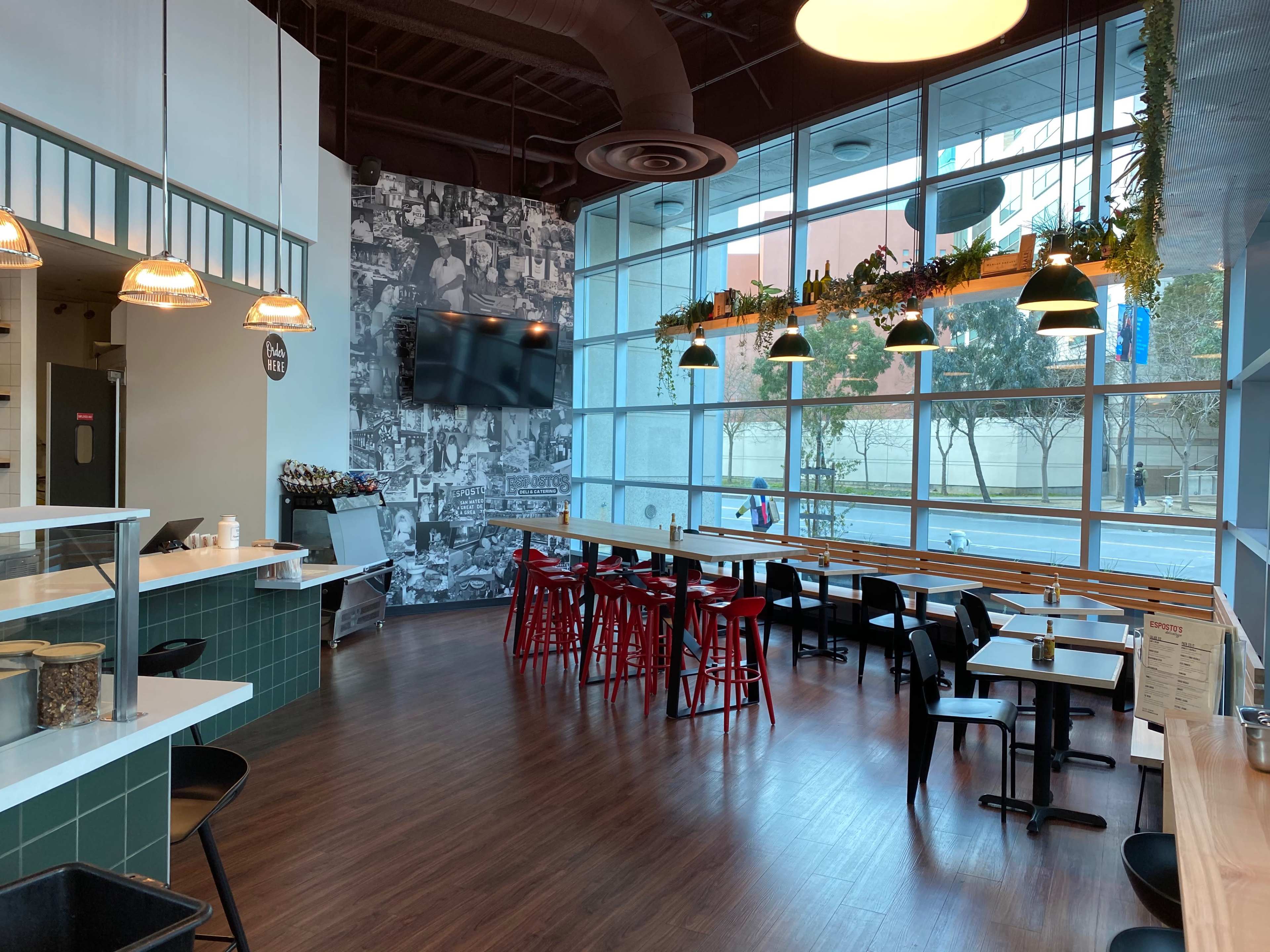 A modern dining area with a mix of black and red chairs, large windows, and a wall covered in black-and-white photos.