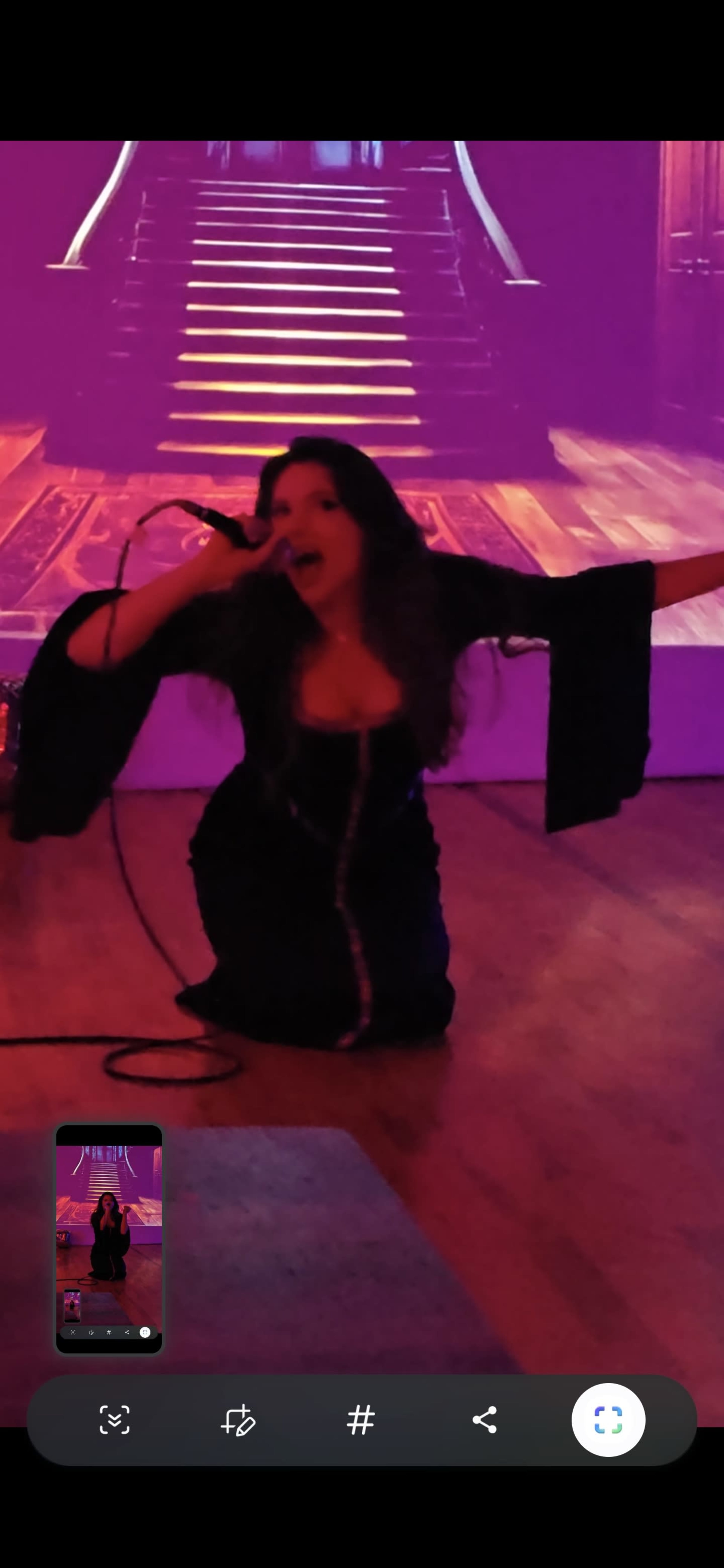 A performer kneels on stage with a microphone, singing in front of a backdrop depicting stairs and a dimly lit room.