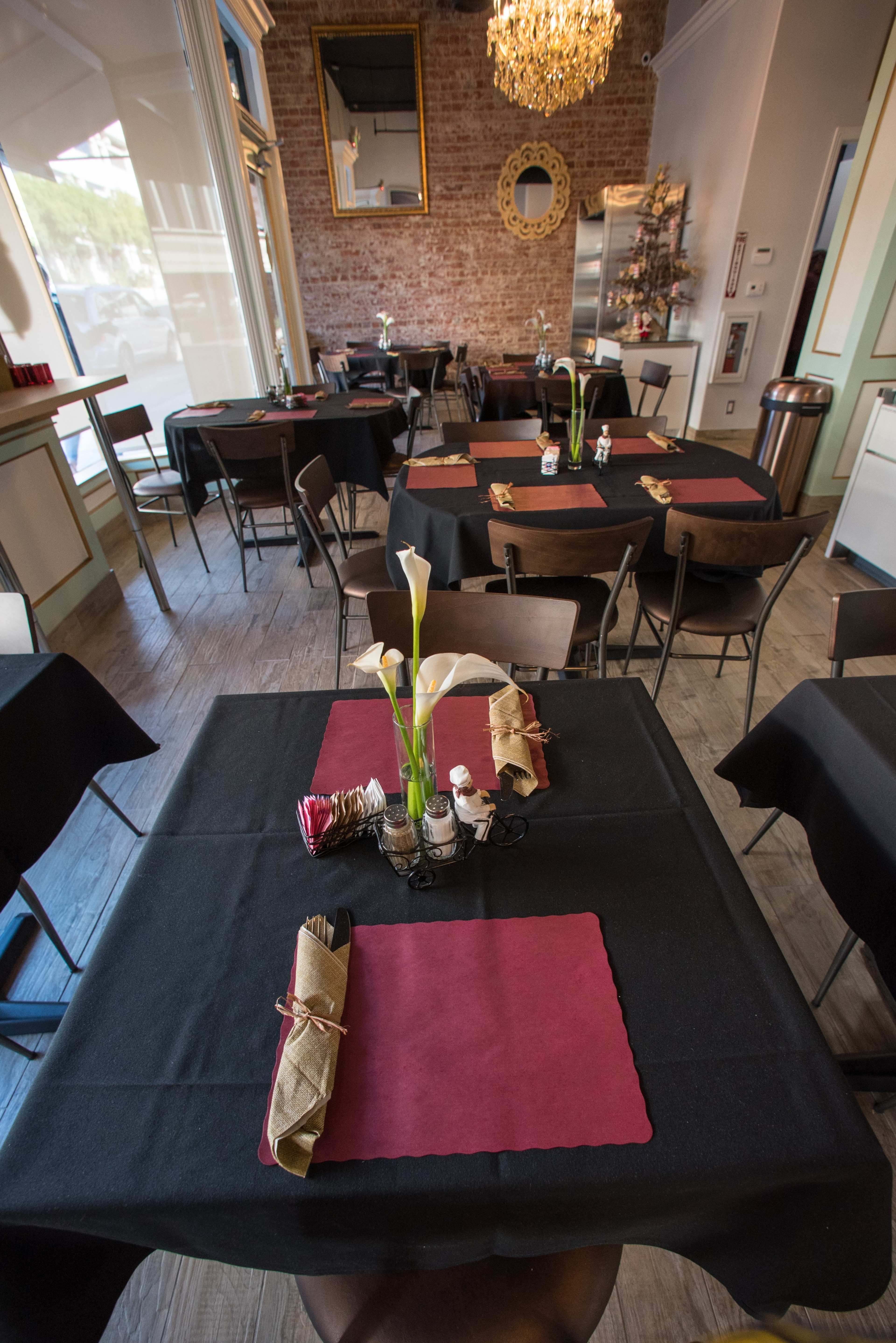 A neatly arranged restaurant interior with black and burgundy table settings and a chandelier overhead.
