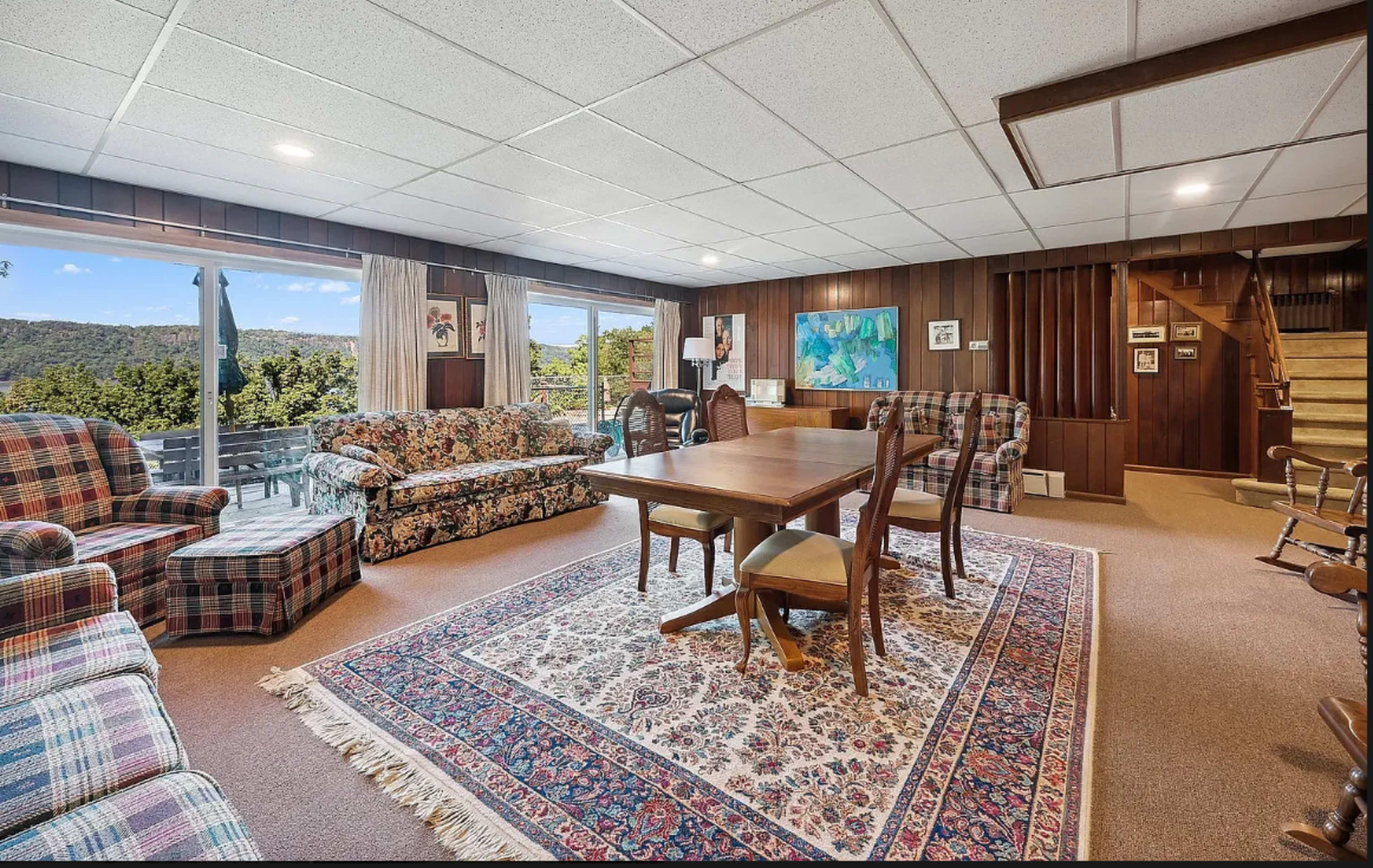 A spacious living area with a dining table surrounded by upholstered chairs, cozy couches, and a large window offering a view of the outdoors.