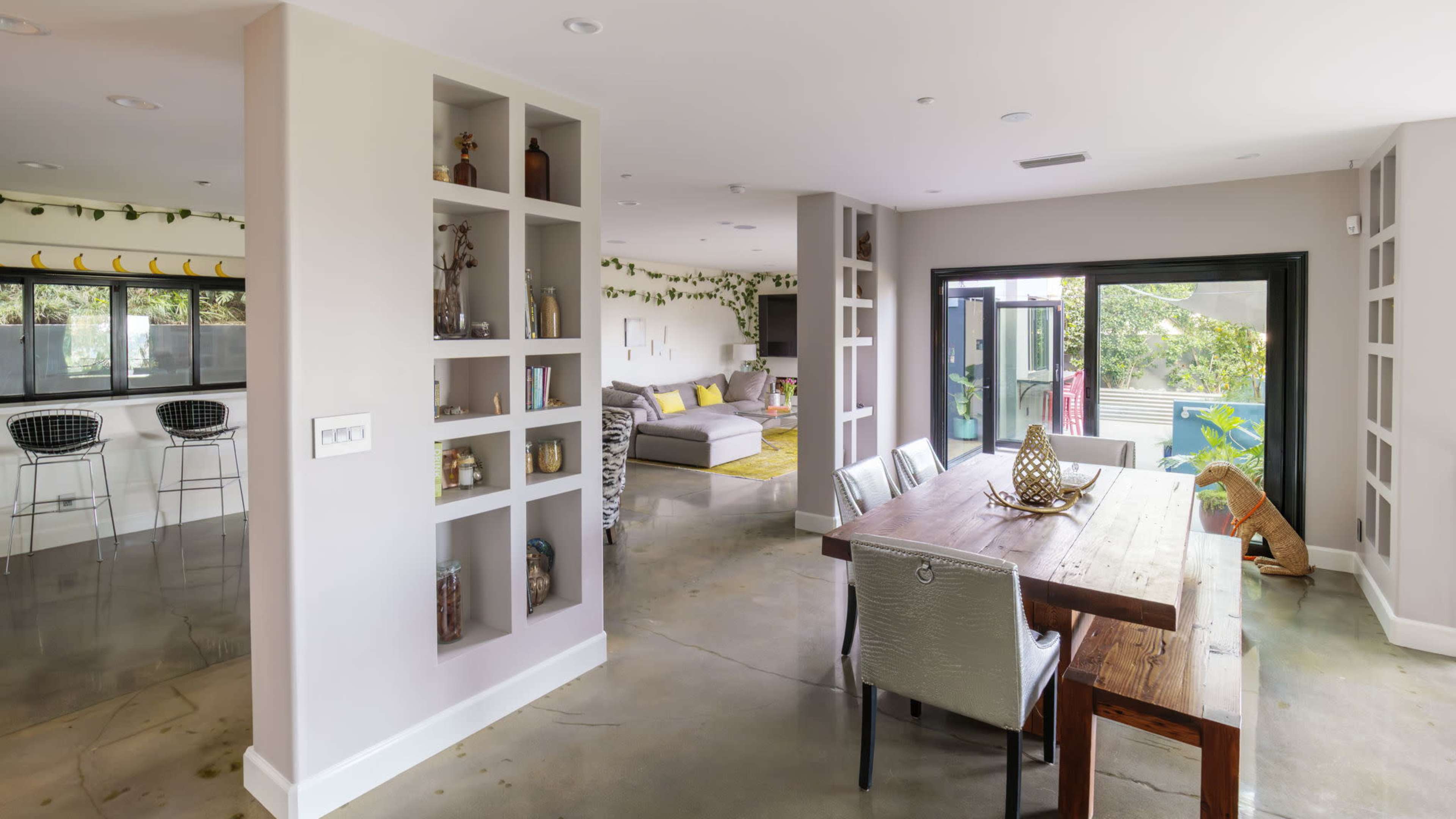 The image features an open-concept living space with a dining area, a modern kitchen bar, and a comfortable seating area, all illuminated by natural light.