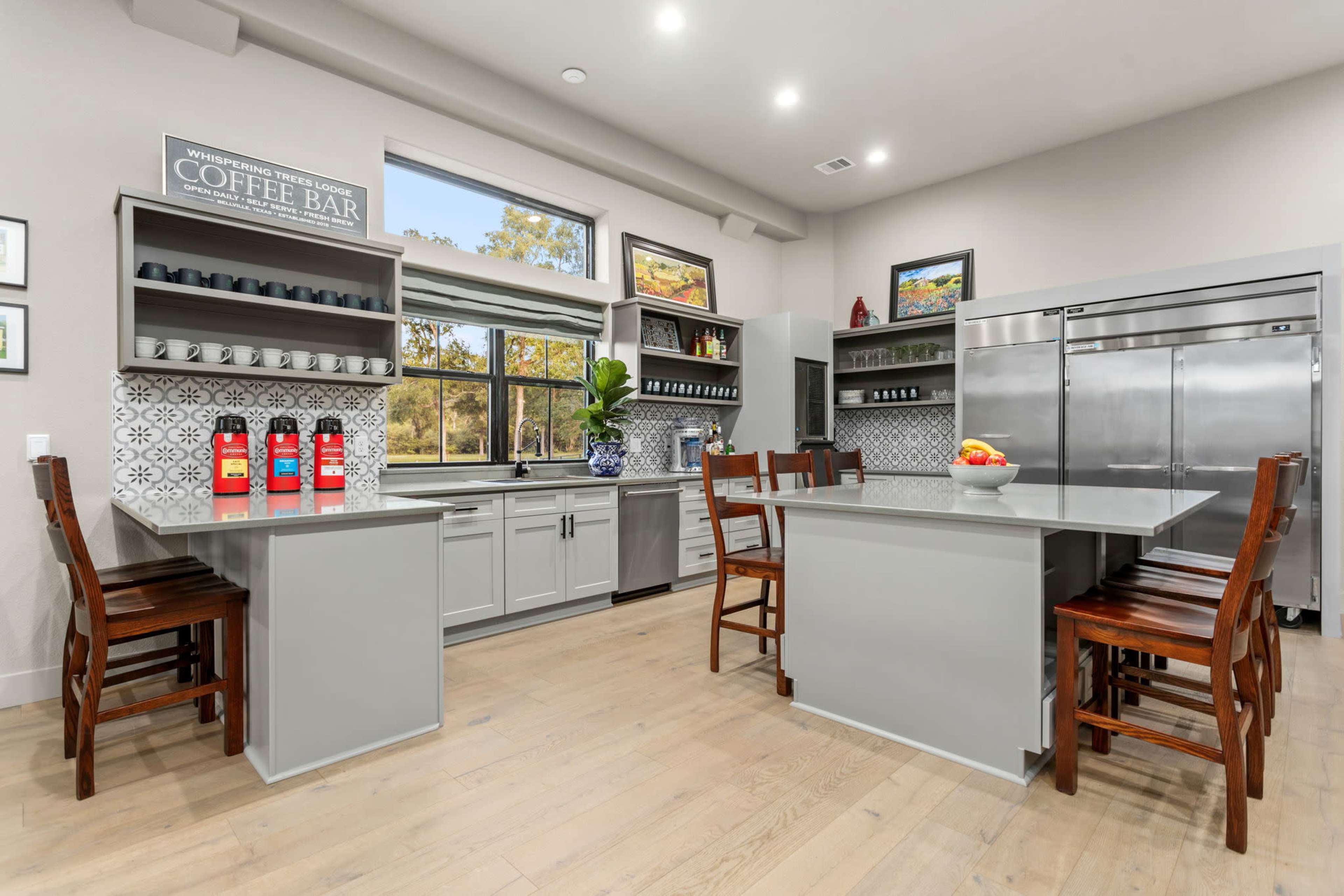 A modern kitchen featuring gray cabinetry, a coffee bar, and stainless steel appliances, with a wooden dining table and chairs.