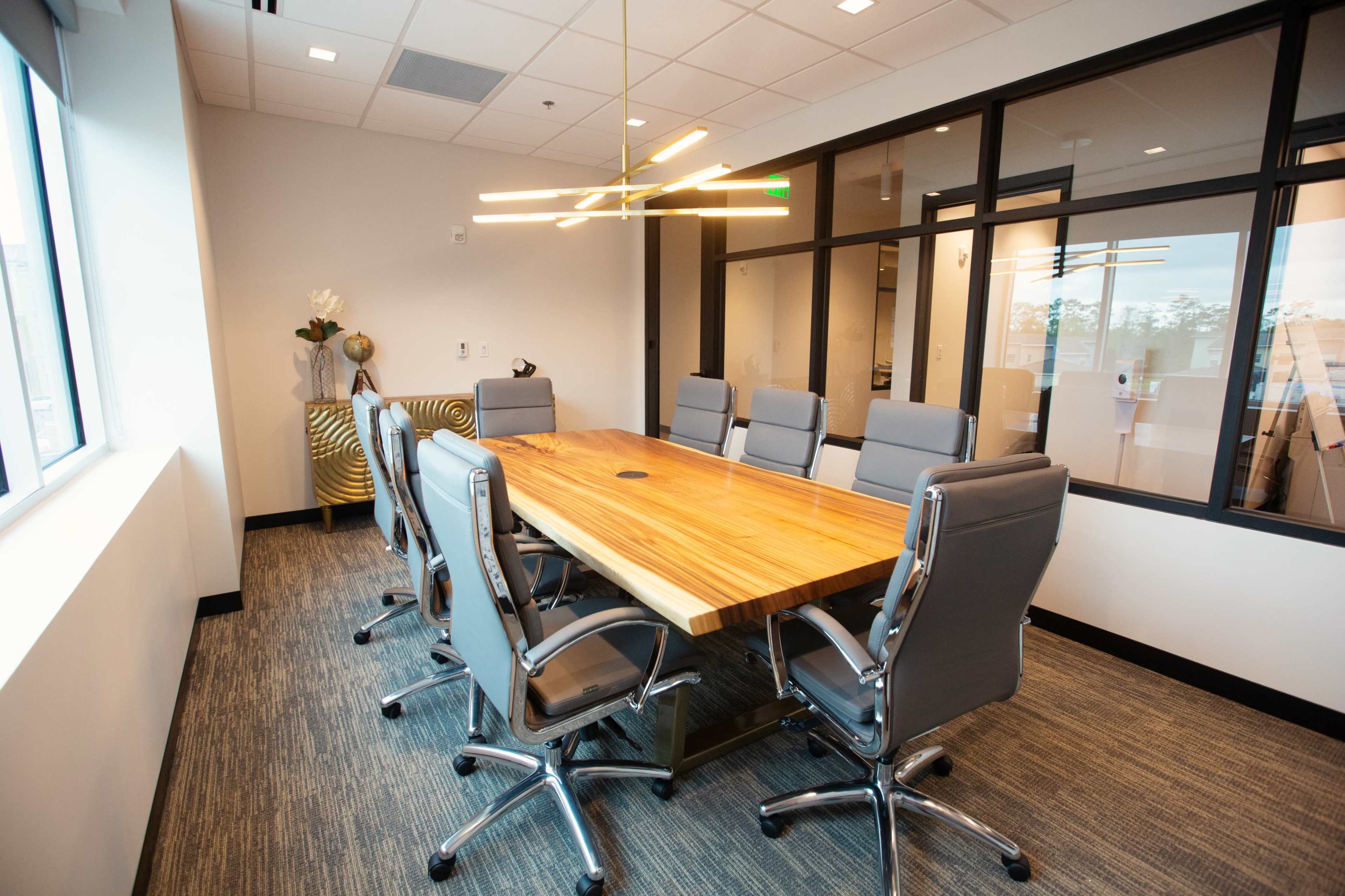 A modern conference room features a large wooden table surrounded by several ergonomic chairs and a stylish light fixture overhead.