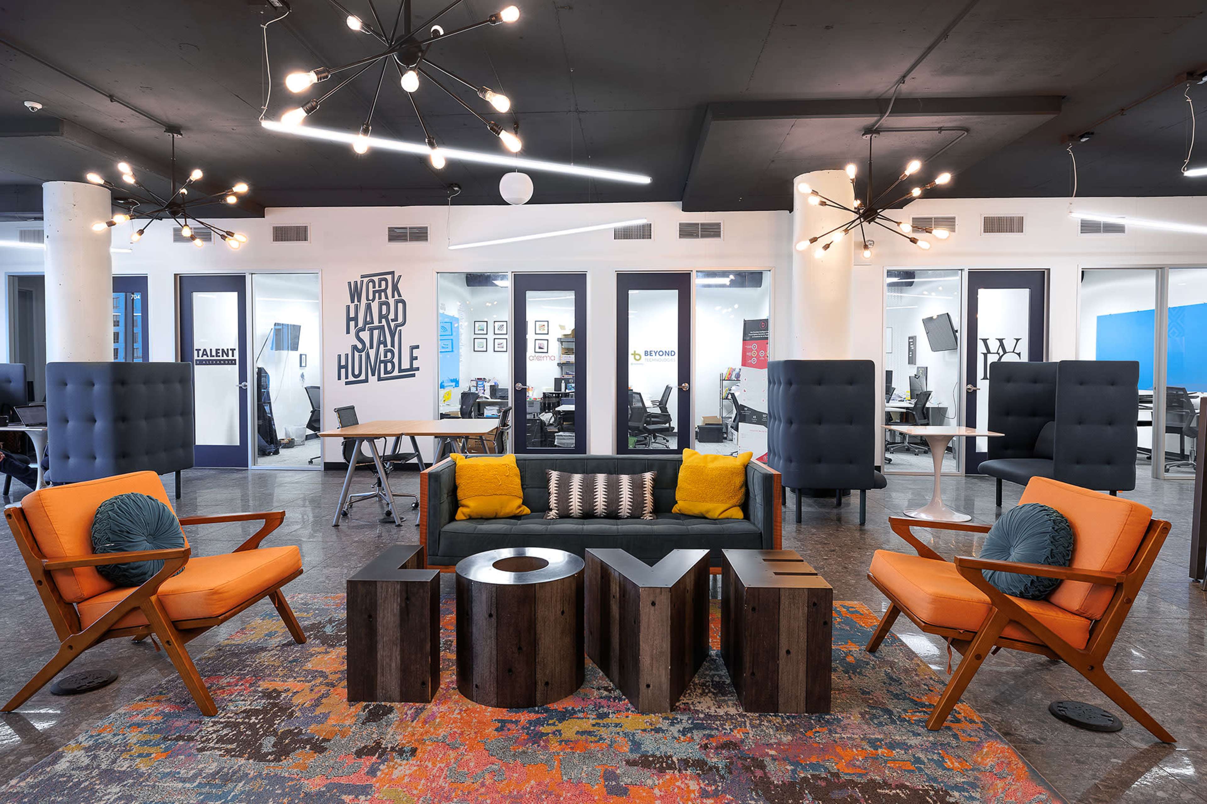 The image shows a modern office space featuring a seating area with orange chairs, a decorative "LOVE" display, and workstations in the background.