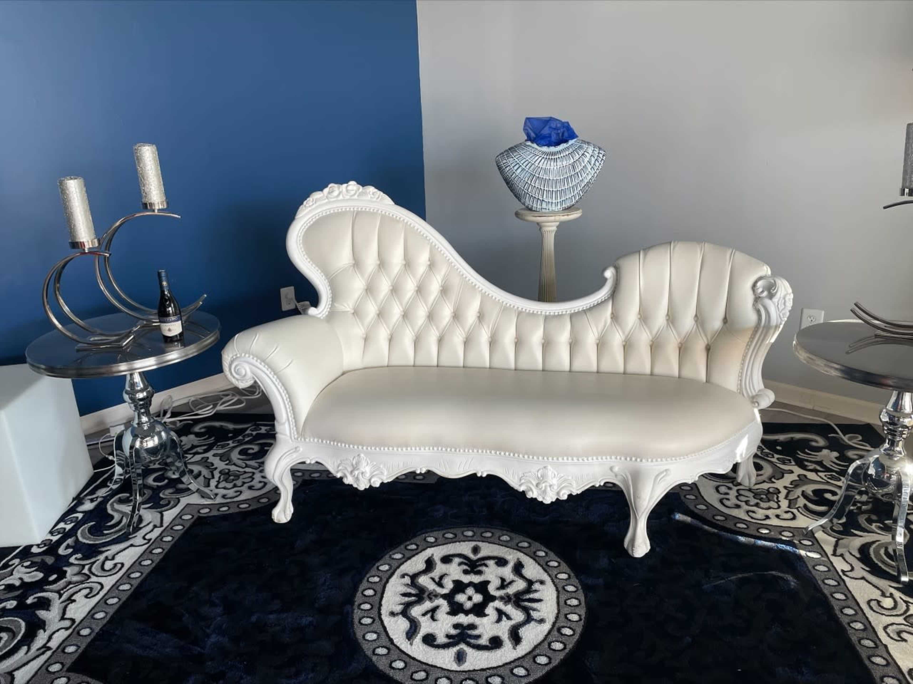 An elegantly designed white sofa with tufted upholstery, placed on a patterned rug, alongside stylish metallic side tables and decorative items.