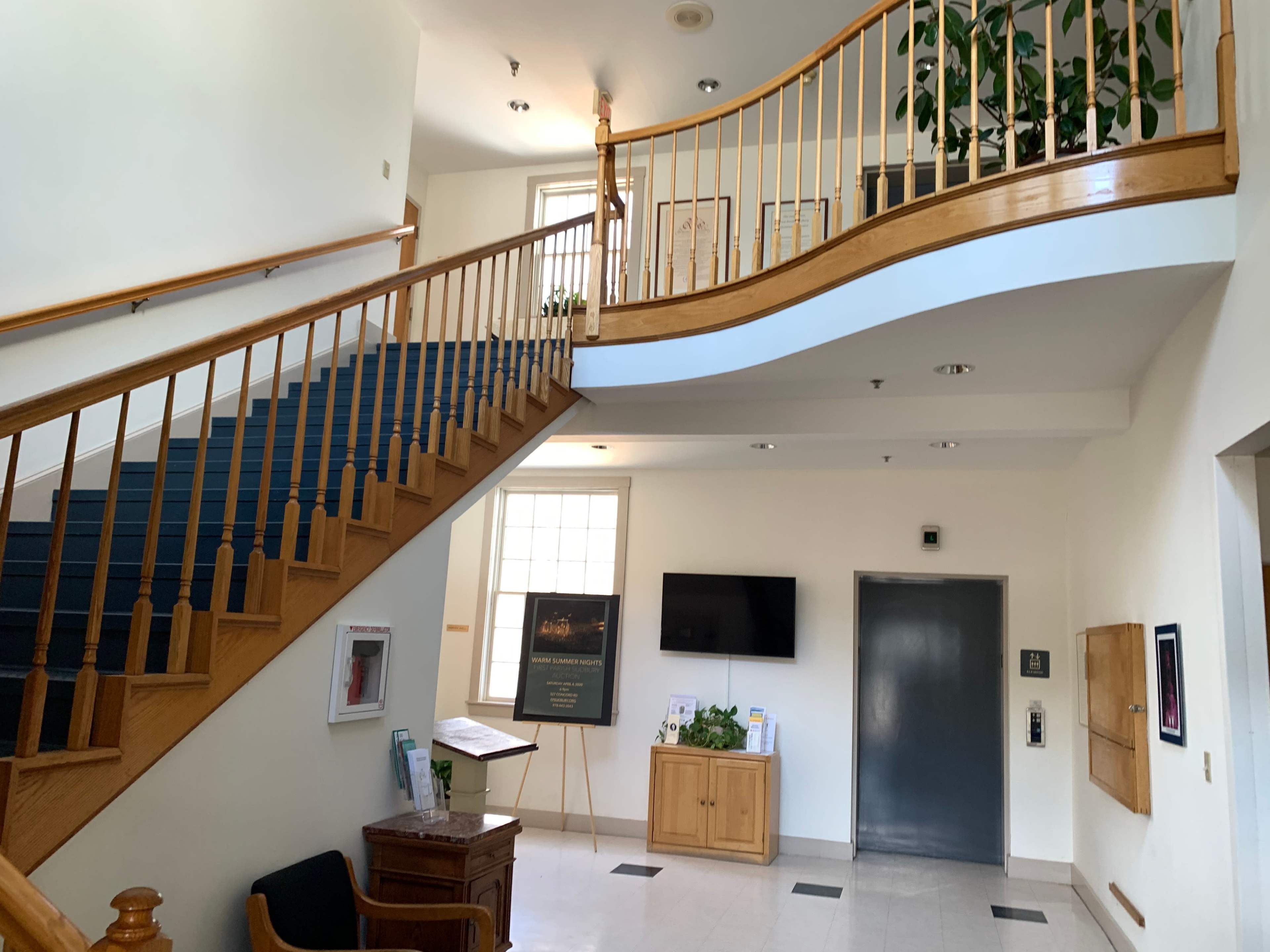 A spacious staircase with wooden railings, leading up to a second floor in a well-lit entryway featuring a television and seating area.