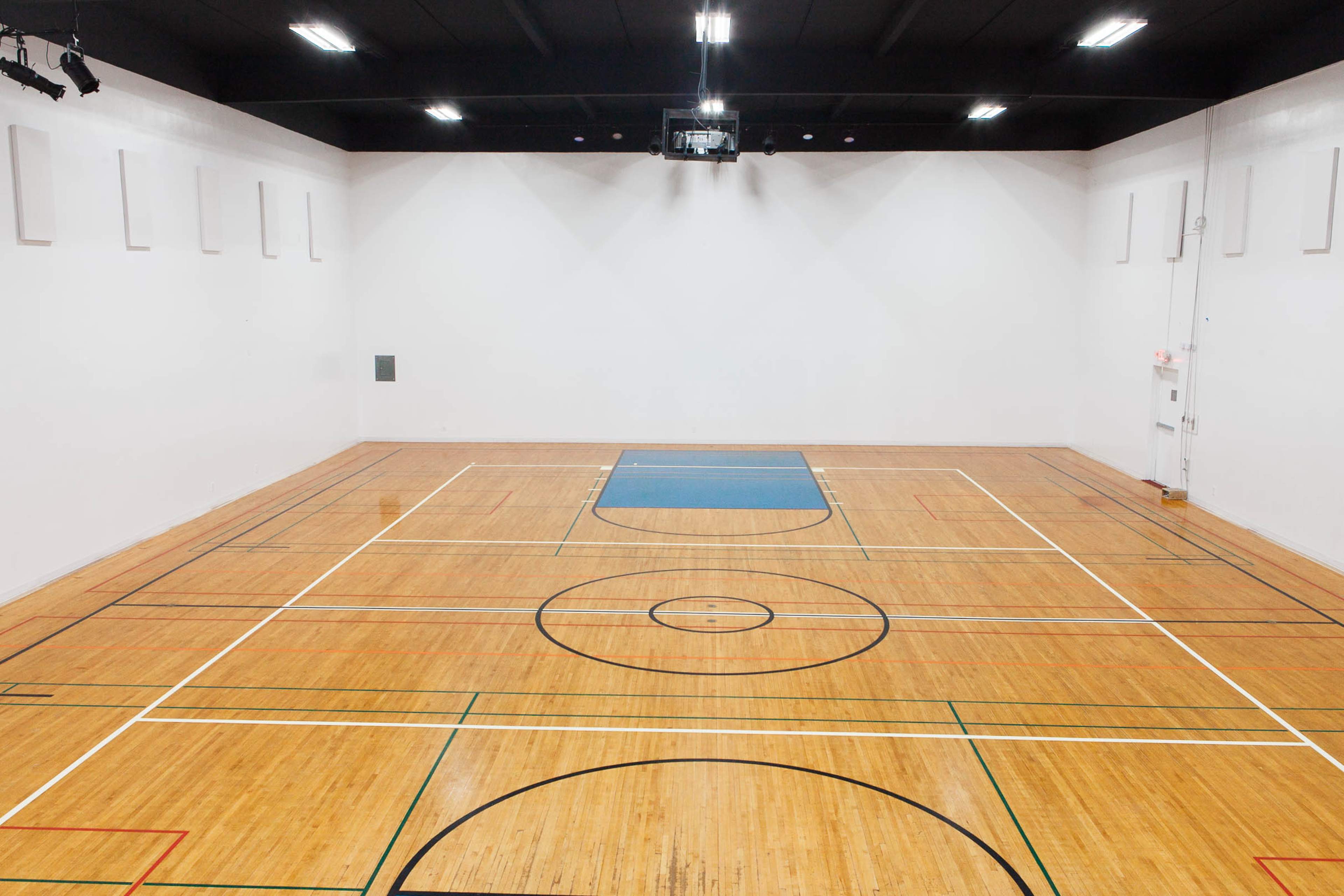 An indoor sports gymnasium with wooden flooring and marked basketball court lines.
